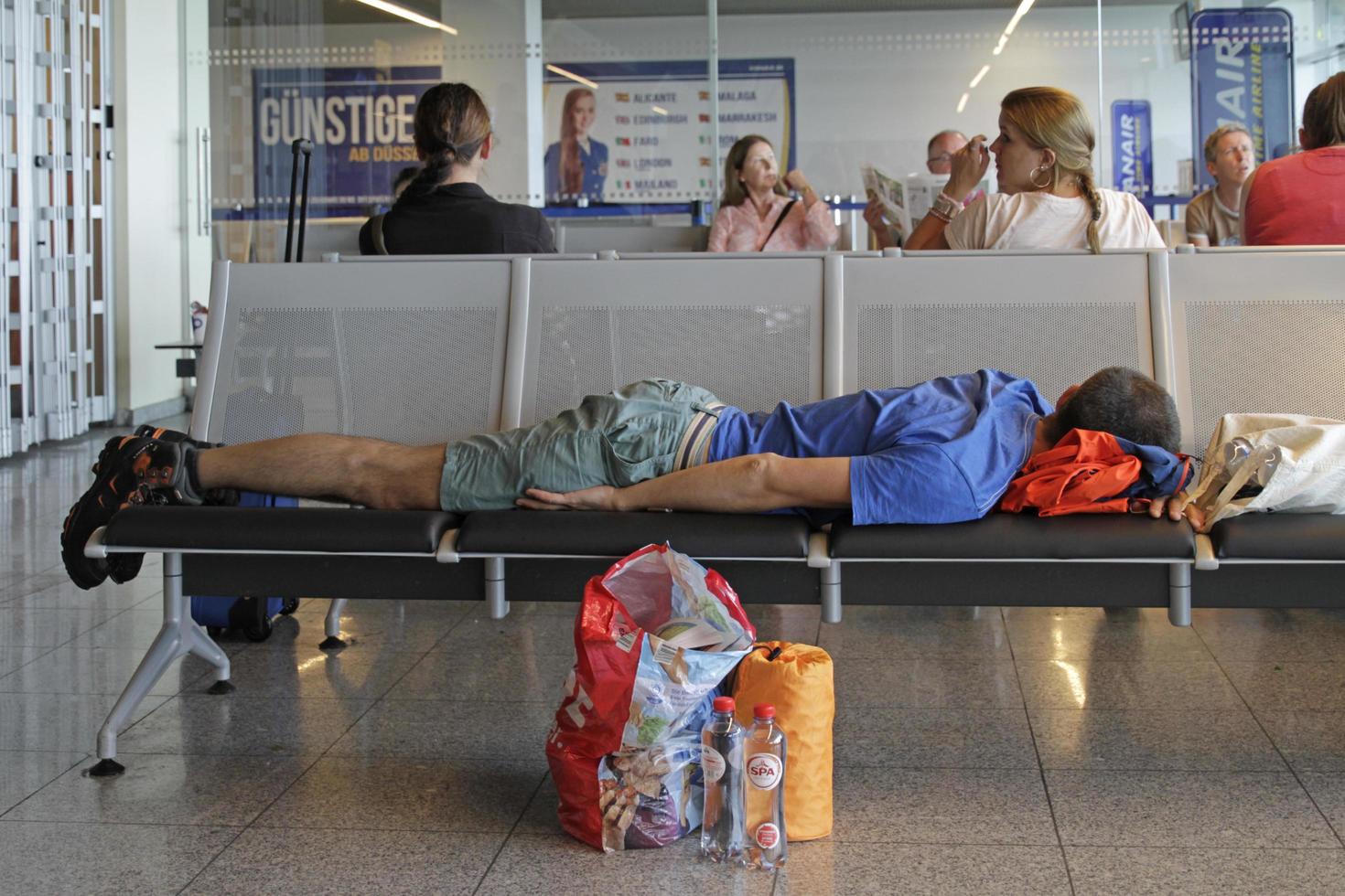 Dusseldorf, Germany - June 23, 2019 - Passenger sleeping on a bench at the airport gate following a flight delay. photo