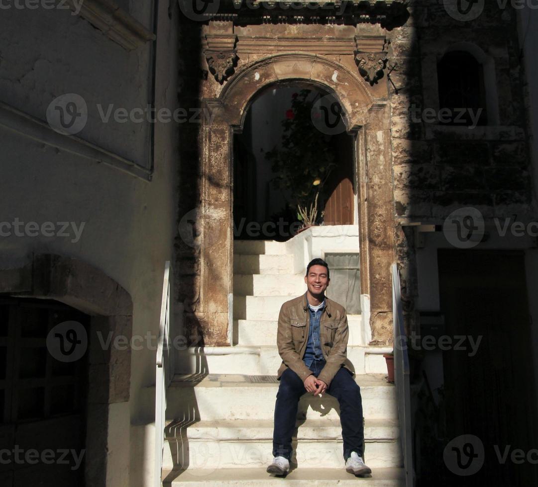 Smiling young man sitting in the sunlight on a flight of stairs to an old building in Italy. photo