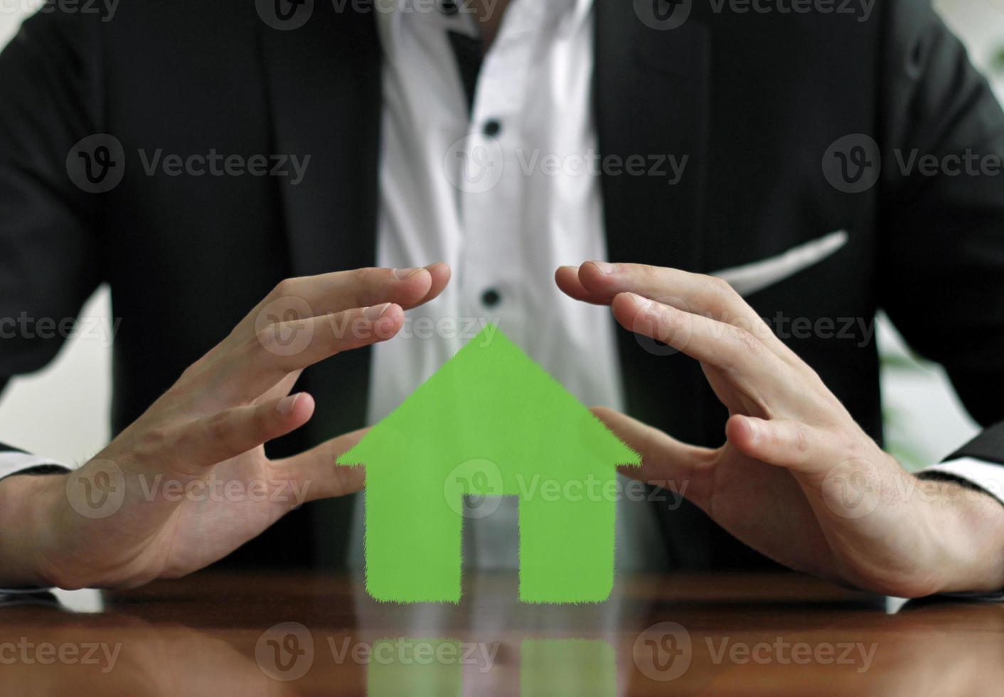 Man protects green colored house with hands photo