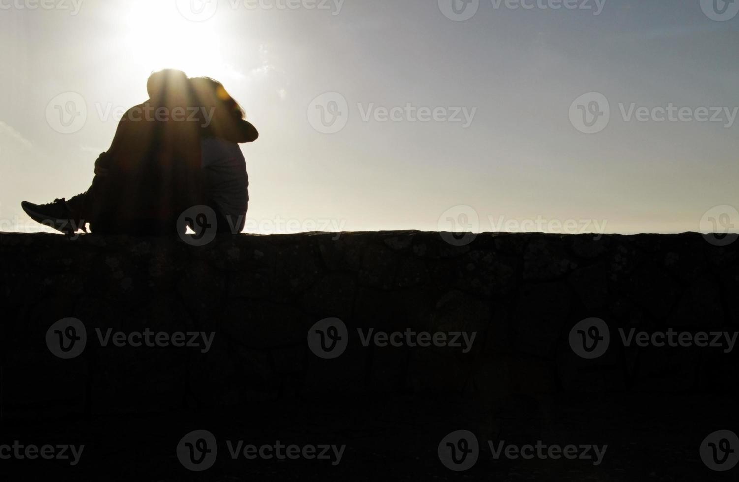 Silhouette of young couple sitting on a wall photo