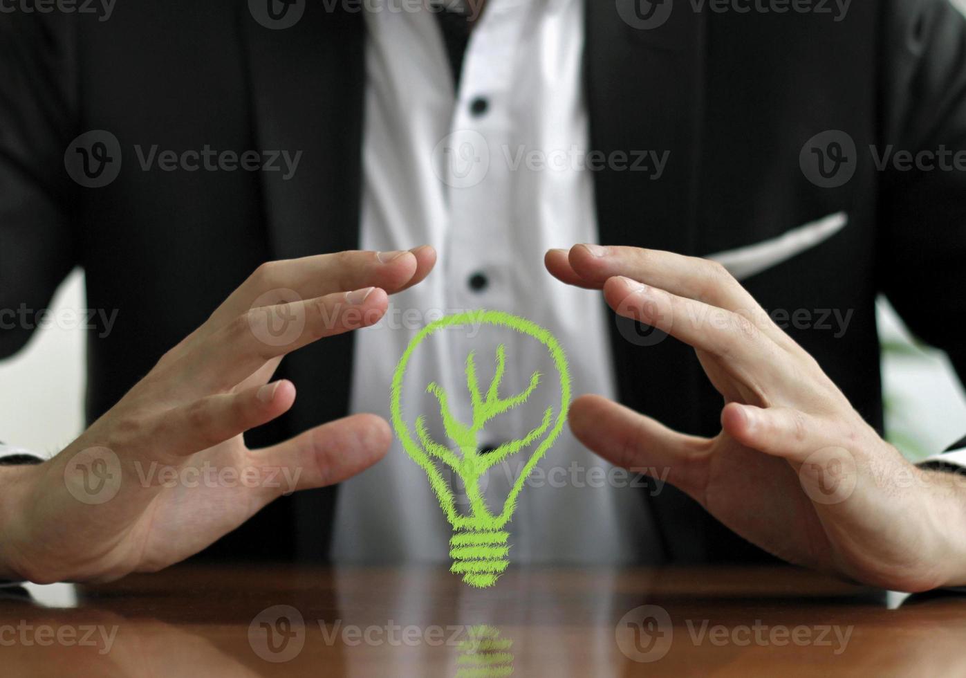 Protecting sustainable energy - businessman with hands around a green light bulb photo