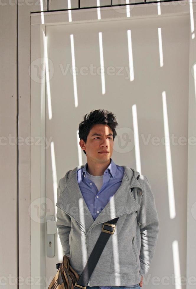 Young man with dark hair standing in front of a wooden wall with sunlight patterns on his face photo