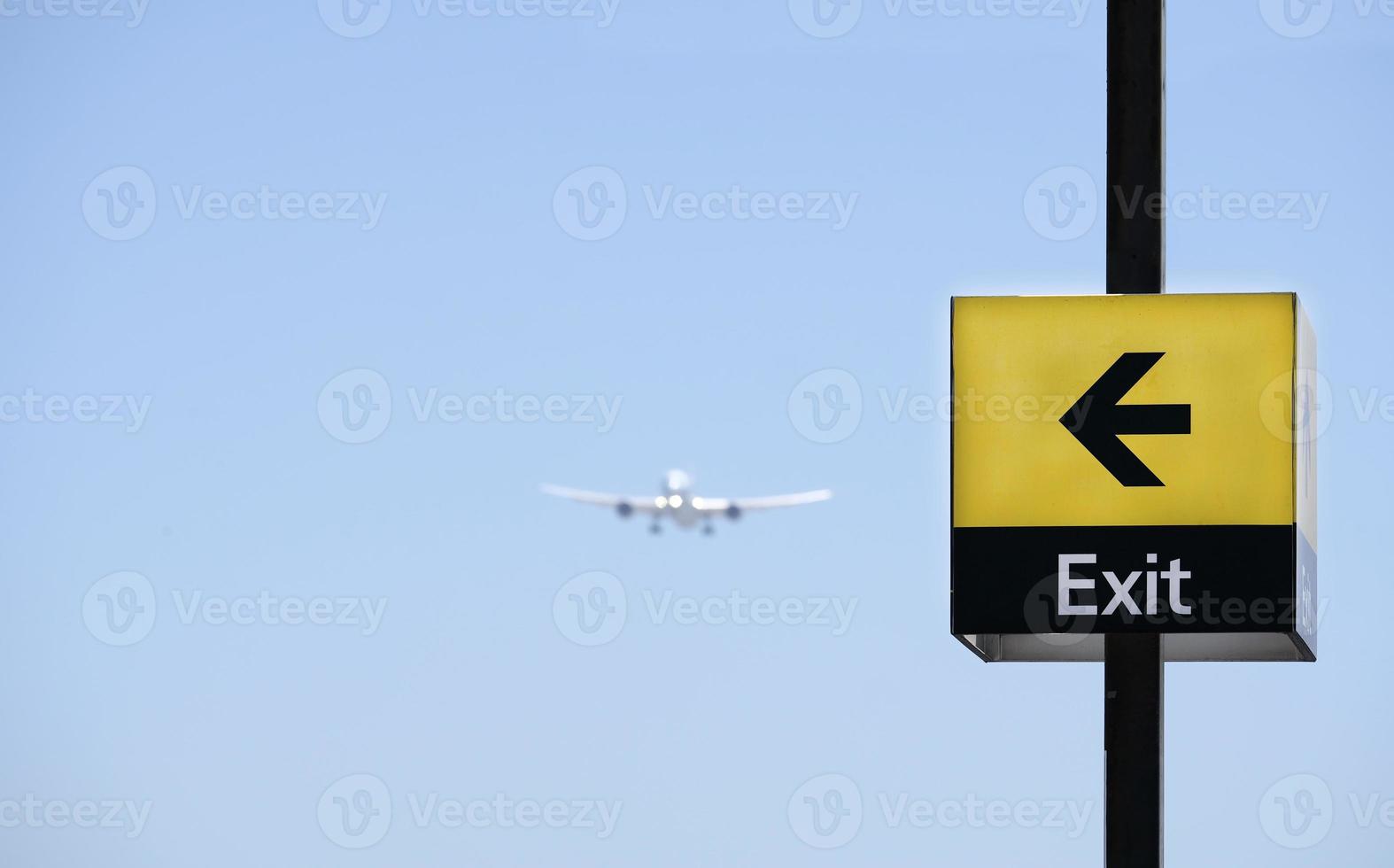 Approaching plane with a sign reading exit pointing at it against a blue sky photo