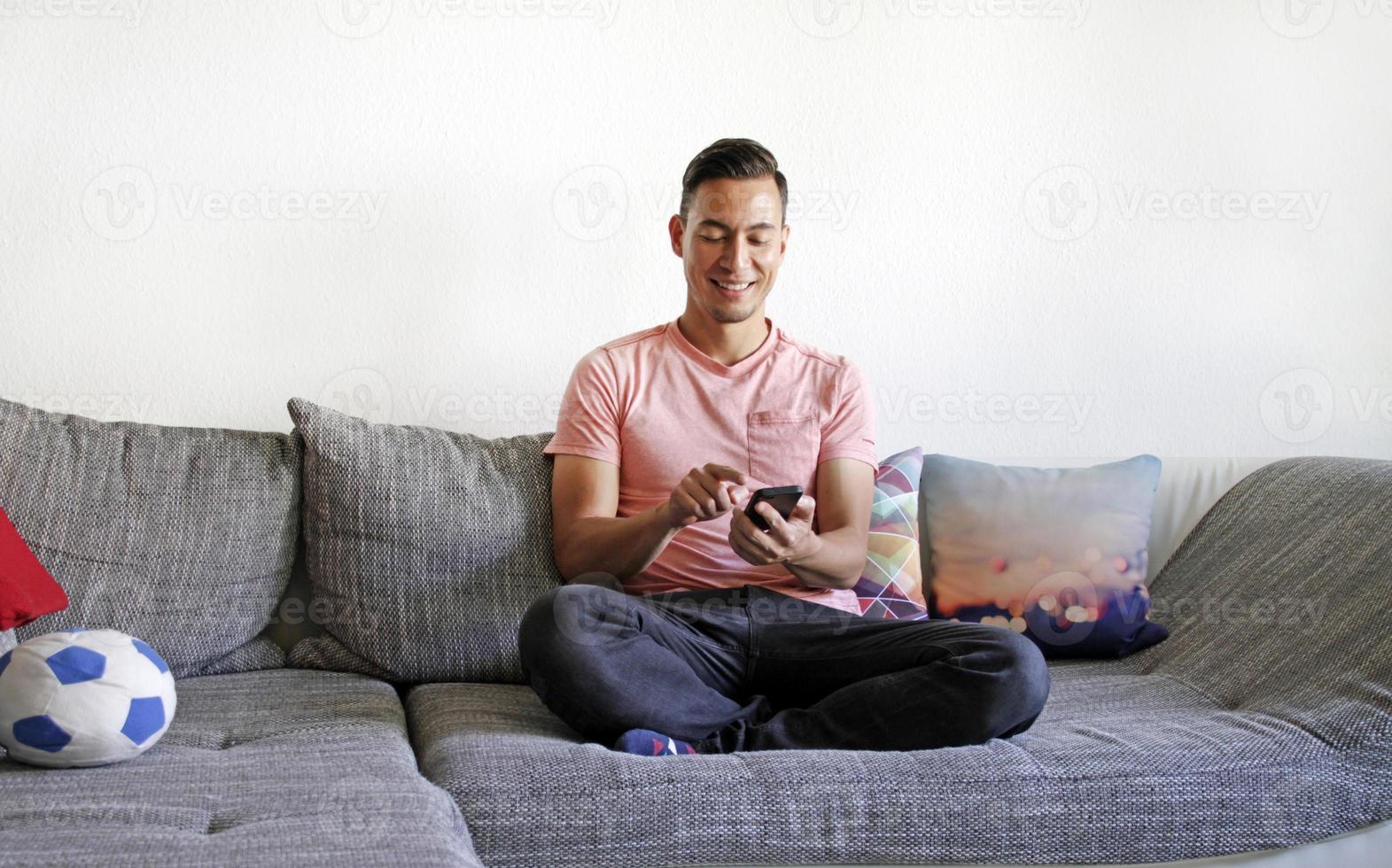 hombre sonriente manejando smartphone mientras está sentado en el sofá foto