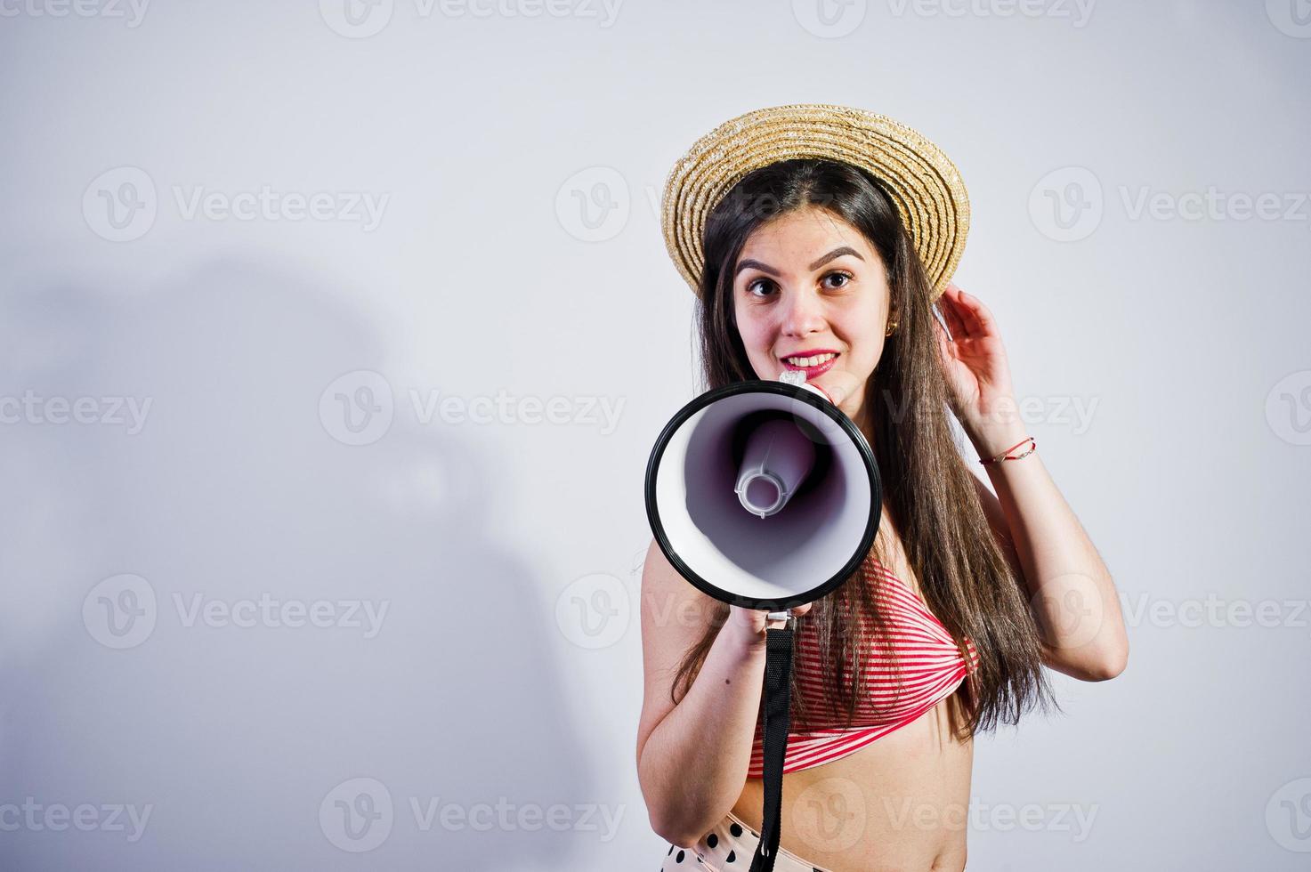 retrato de una hermosa joven en traje de baño y sombrero habla por megáfono en el estudio. foto