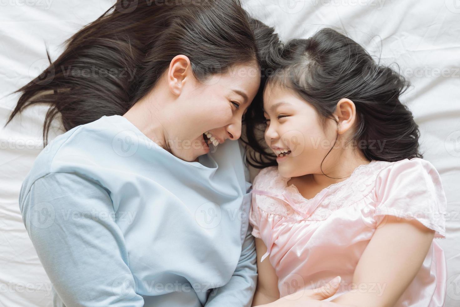 madre y su hija niña jugando en el dormitorio. feliz familia asiática foto