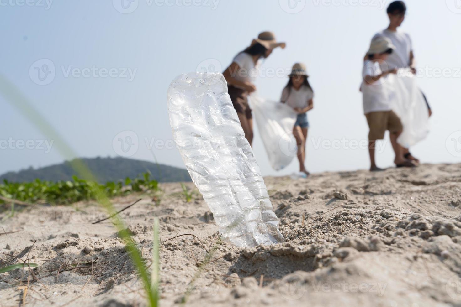 Asian Family volunteer picking up a plastic bottle on a beach with a sea to protect an environment photo