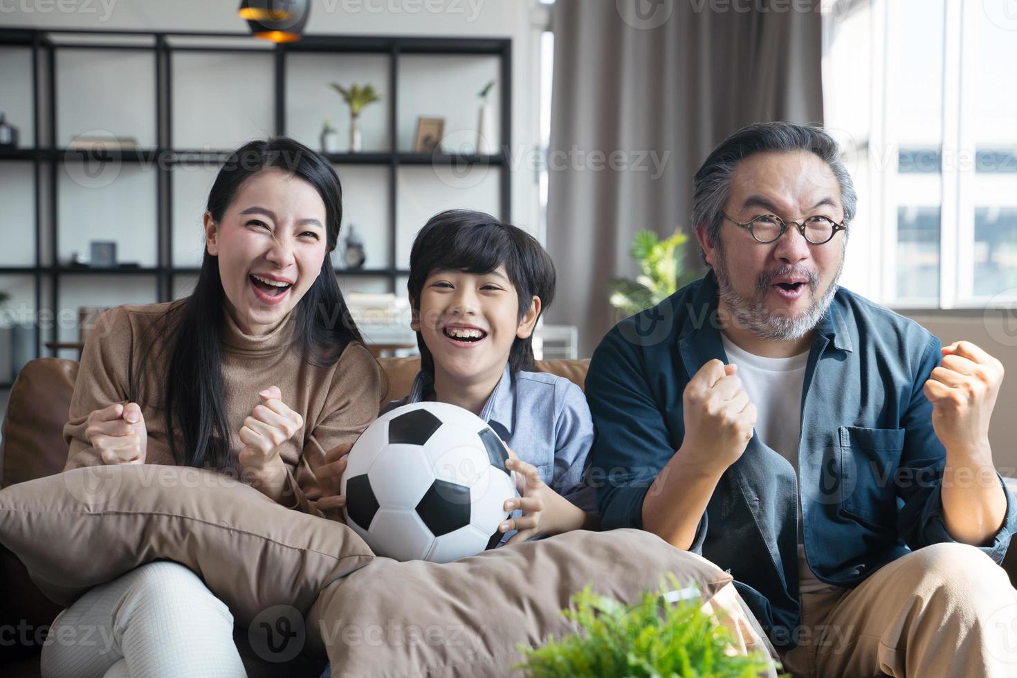 familia asiática viendo partidos de fútbol en la televisión y reaccionando feliz saliendo cuando el equipo dispara la pelota al gol. foto