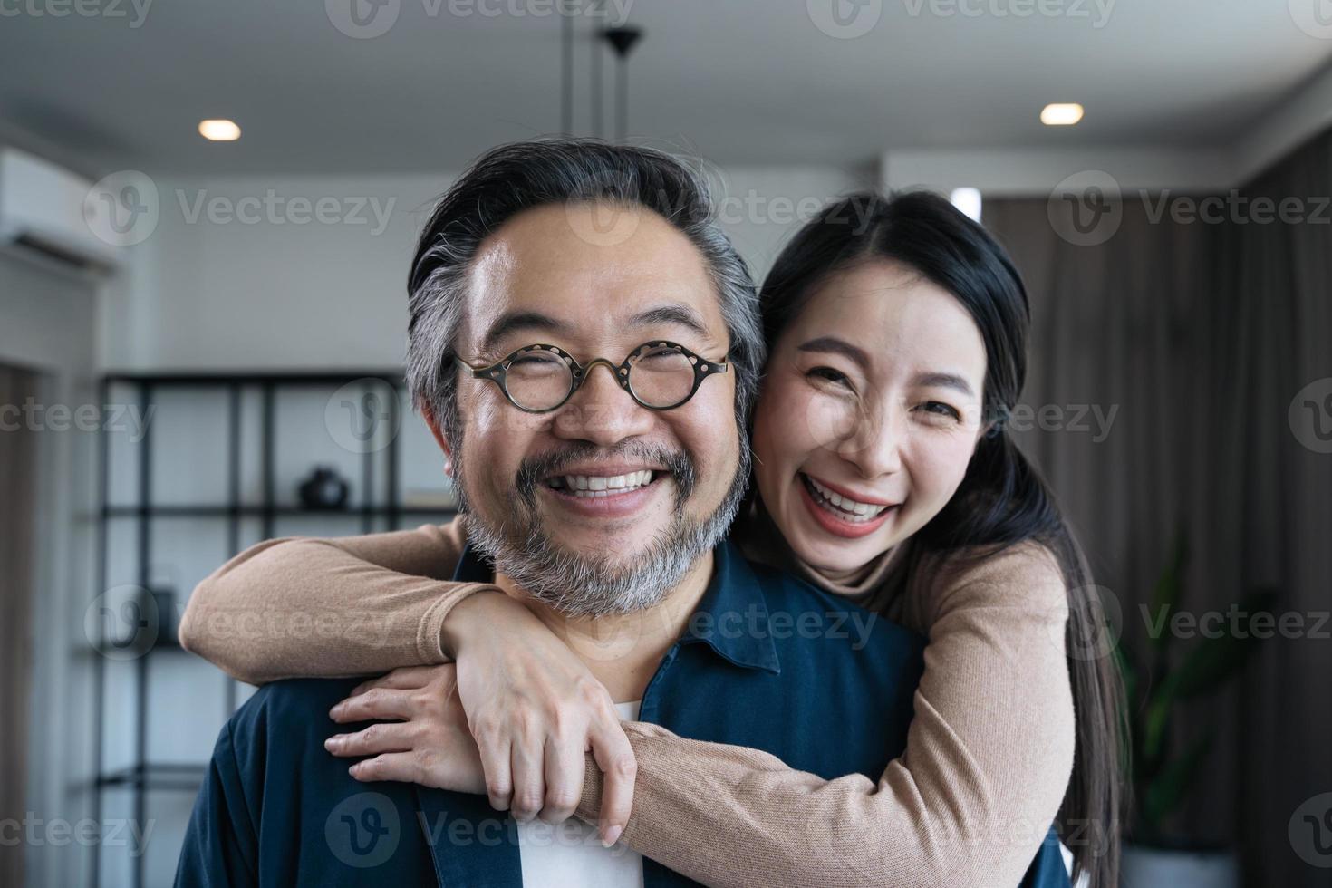primer plano pareja asiática de mediana edad sonriendo para la cámara y mirándose el uno al otro. retrato de pareja familiar foto