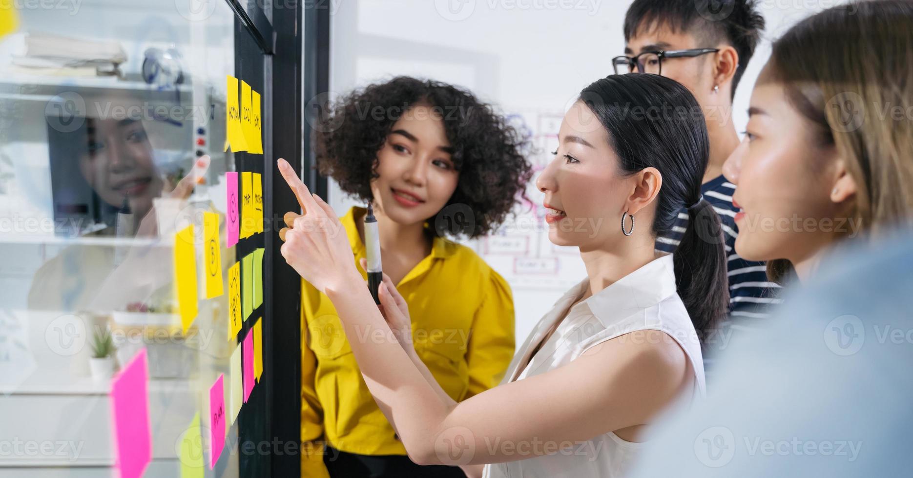 Group of Asian business people meeting at modern office .Young creative team use post it notes to share idea sticky note on glass wall. and working design planning and Brainstorming concept. photo