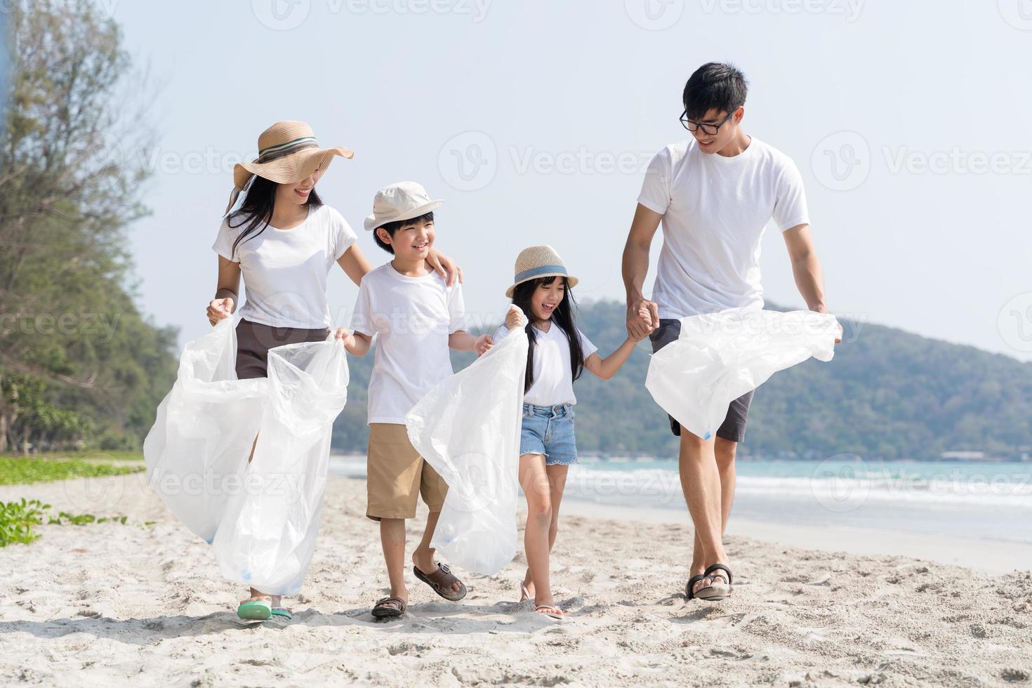 voluntario familiar asiático recogiendo una botella de plástico en una playa con mar para proteger el medio ambiente foto