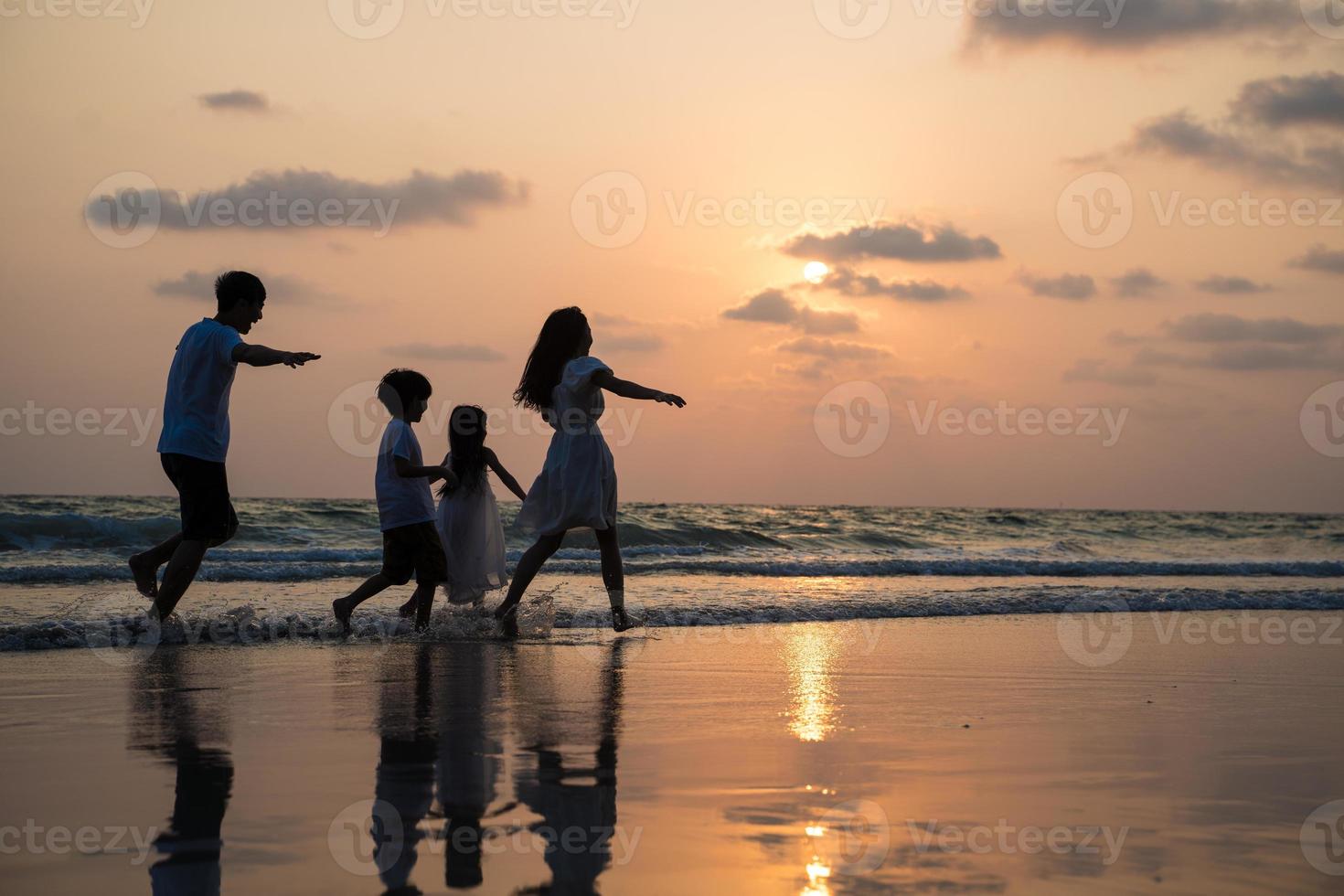 silueta familia caminando y jugando al atardecer en la playa con niños felices vacaciones concepto foto