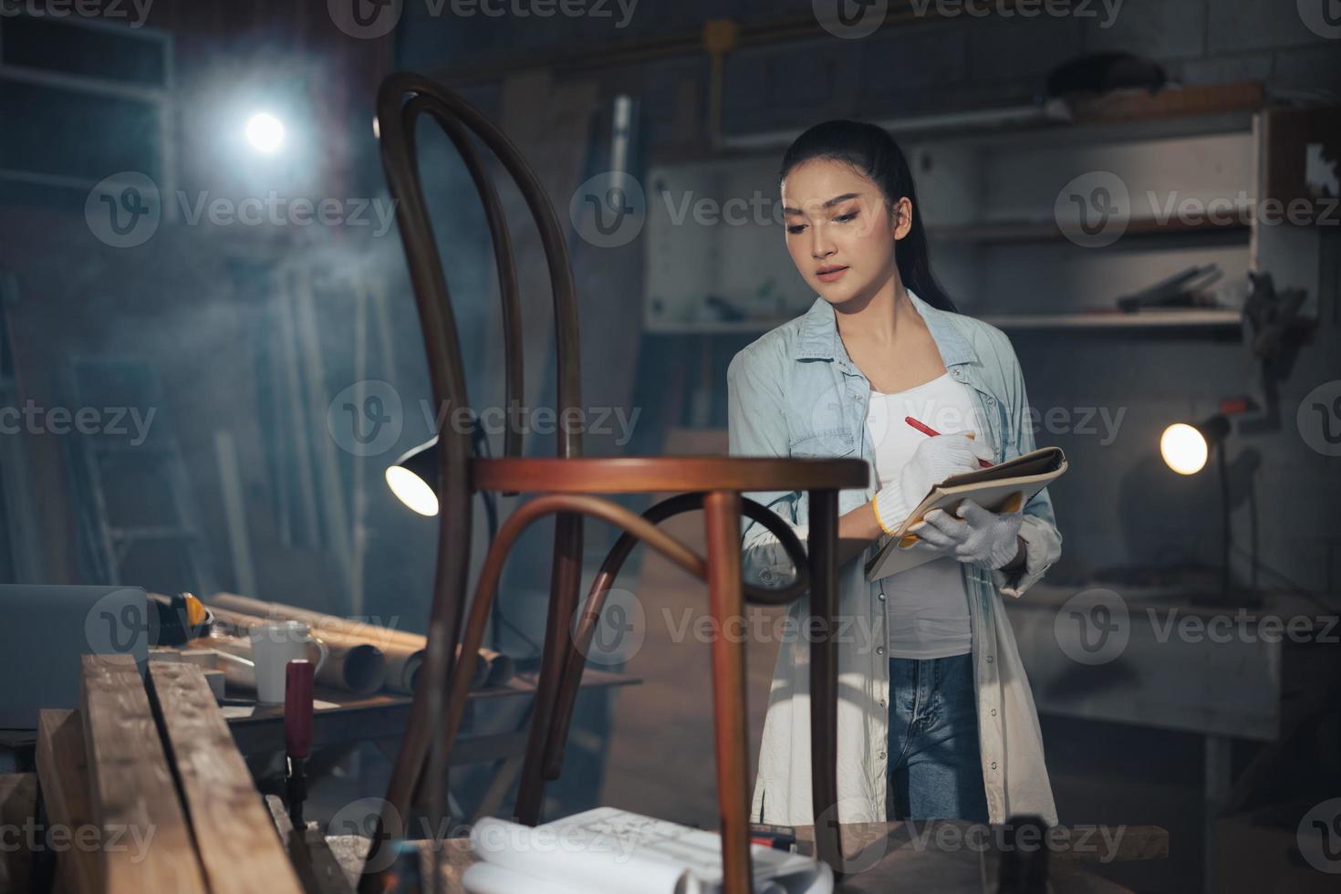 La joven carpintera asiática de diseñador de muebles usa una cinta métrica para medir la silla en el banco de trabajo en el taller de carpintería de madera. foto
