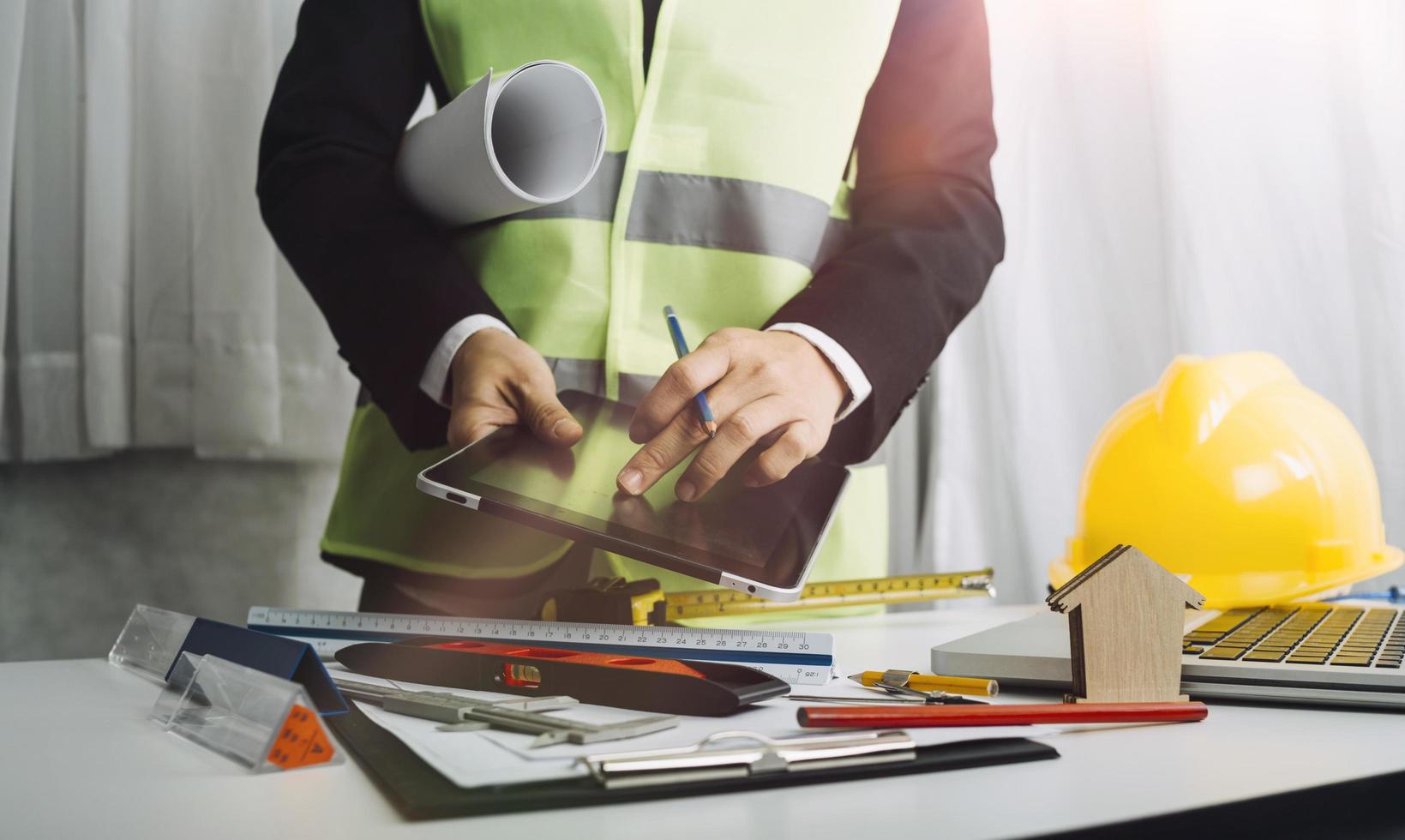 Dos colegas discutiendo el trabajo de datos y una tableta, un portátil con un proyecto arquitectónico en el sitio de construcción en un escritorio en la oficina foto