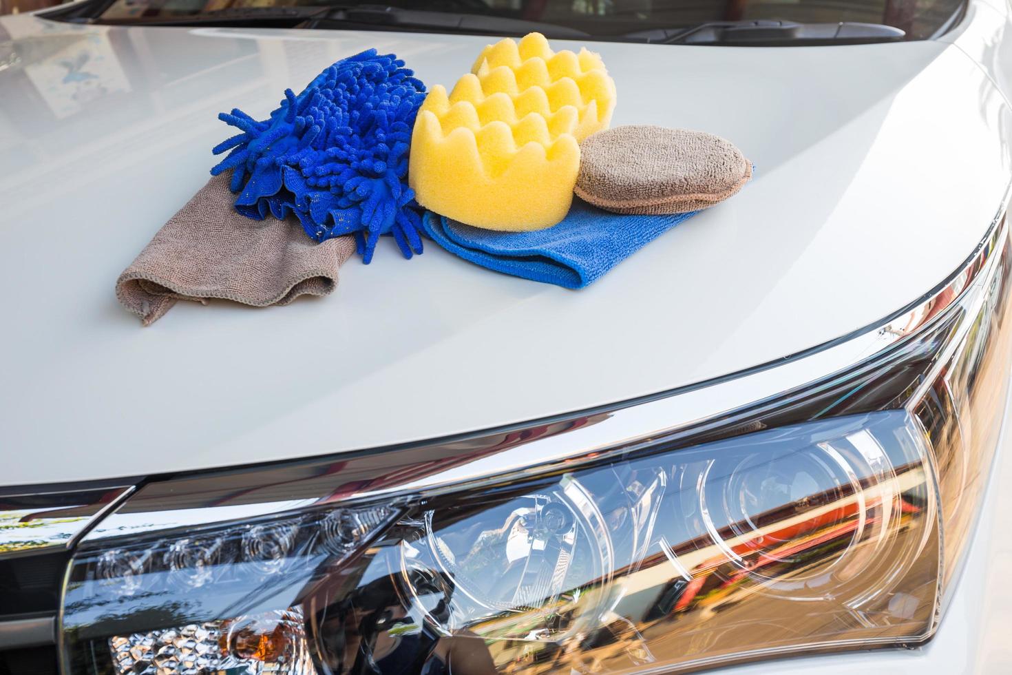 Yellow, green sponges and blue mitts for washing and microfiber fabric with cleaner cloth on white car photo