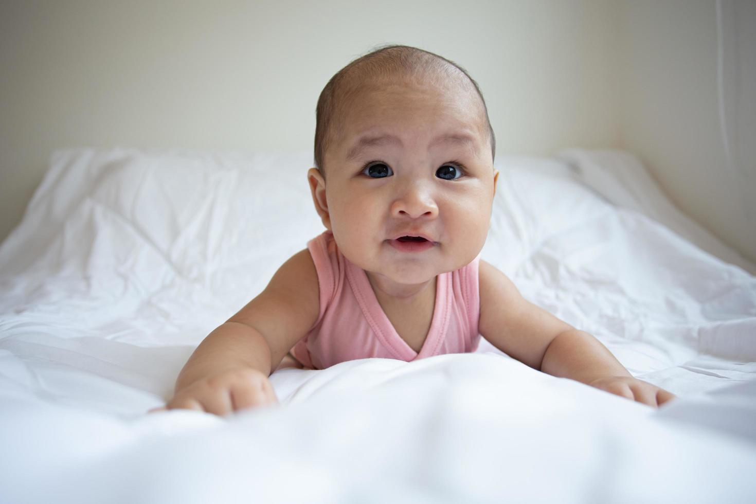 lindo bebé asiático en dormitorio blanco soleado. niño recién nacido descansando en la cama foto