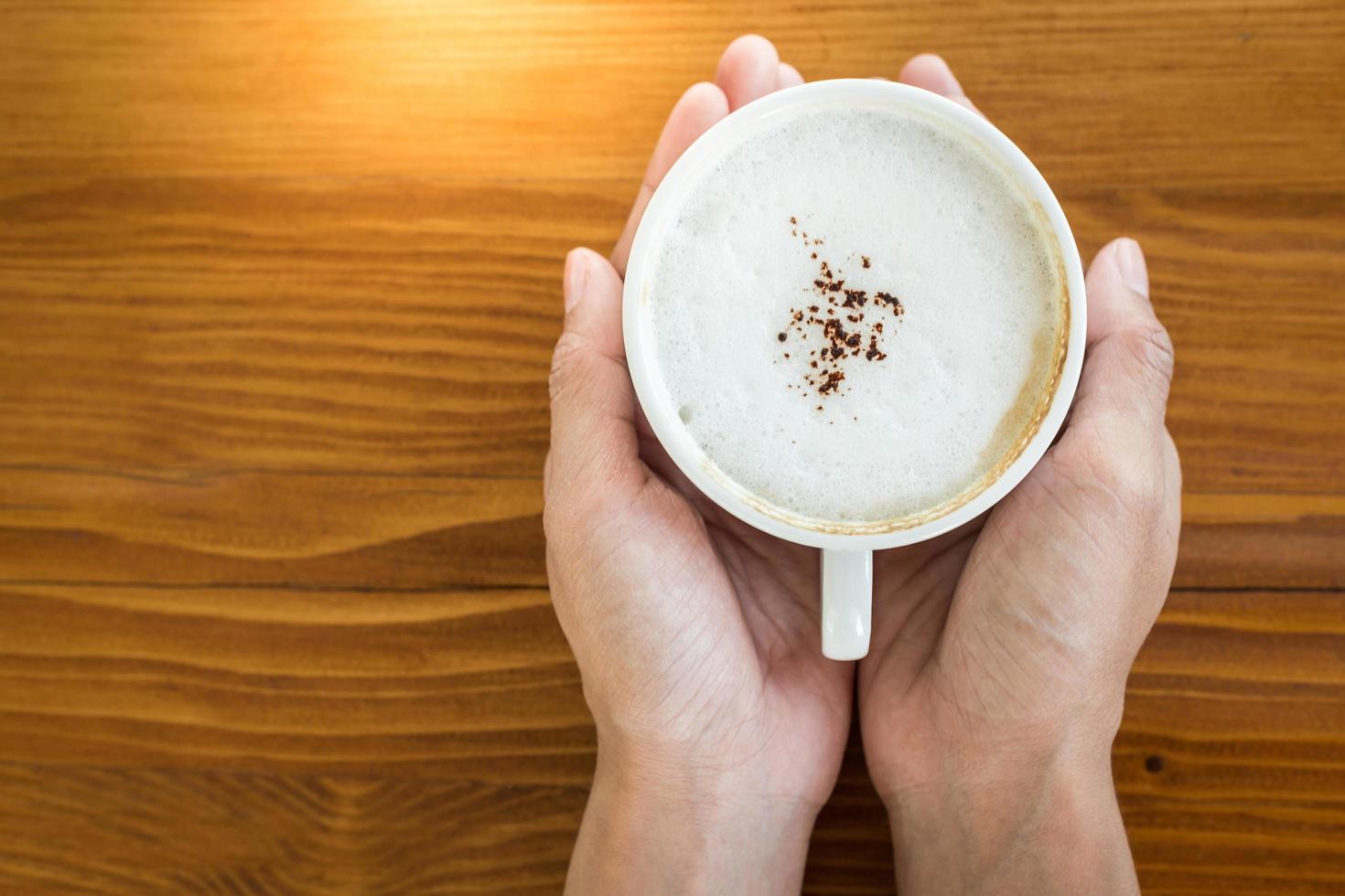 Female hands holding cups of coffee on wooden table. Copy space background for text photo