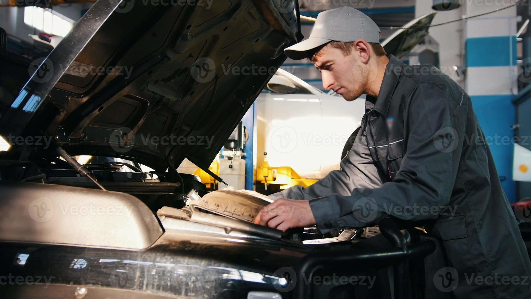 Mecánico masculino en diagnóstico de motor de procesamiento de garaje de automóviles - comprobando en el capó del coche para suv de lujo foto