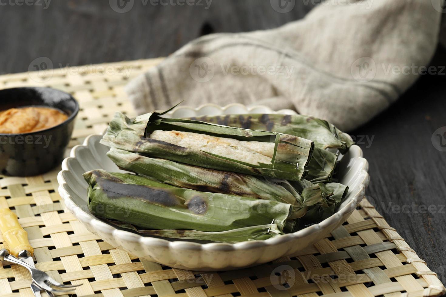 otak otak asado, pastel de pescado indonesio envuelto con hoja de plátano y parrilla. servido con salsa de maní o salsa picante roja dulce y salada foto