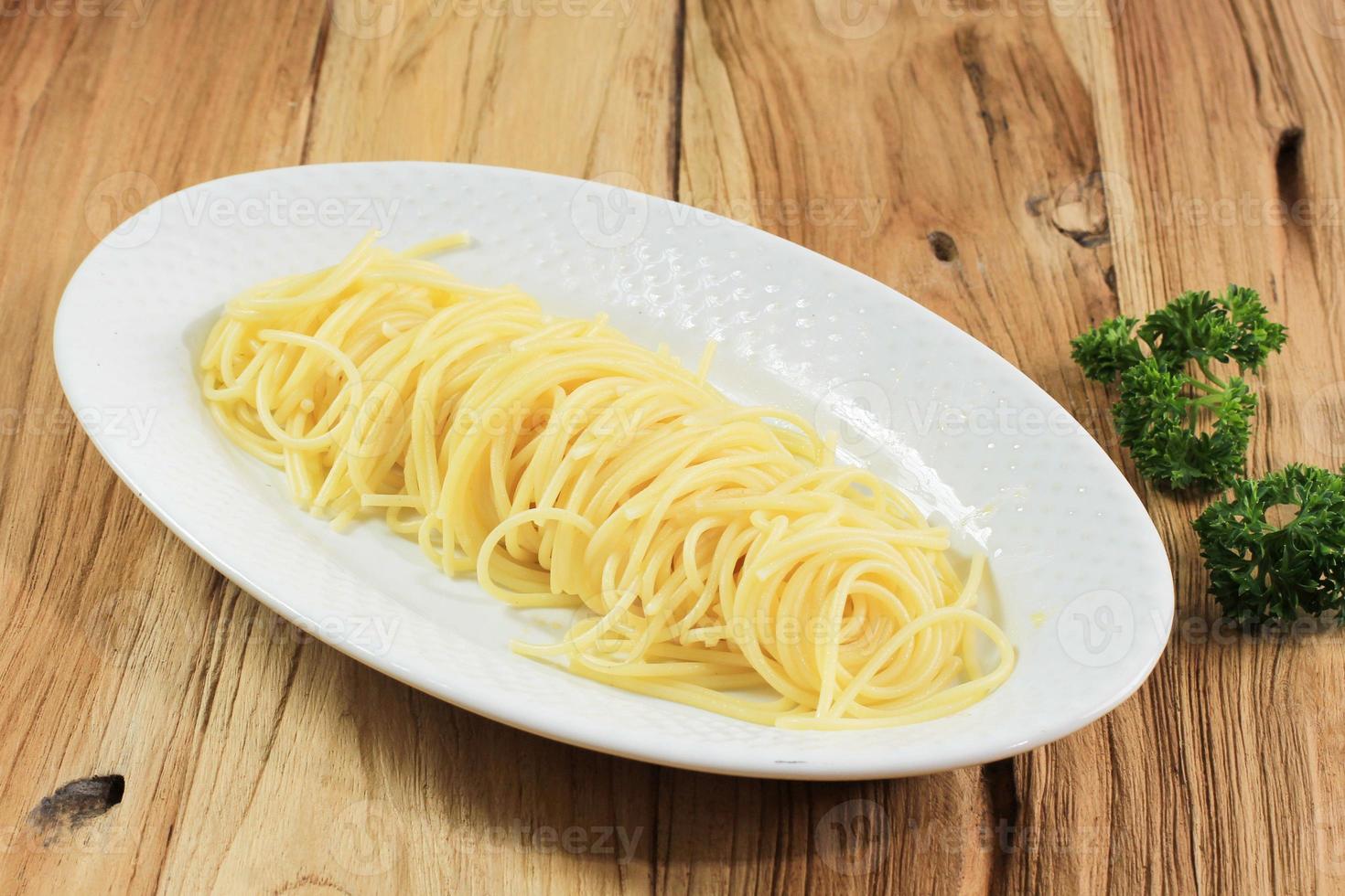 Pasta de espagueti en un plato blanco ovalado aislado sobre fondo de madera foto