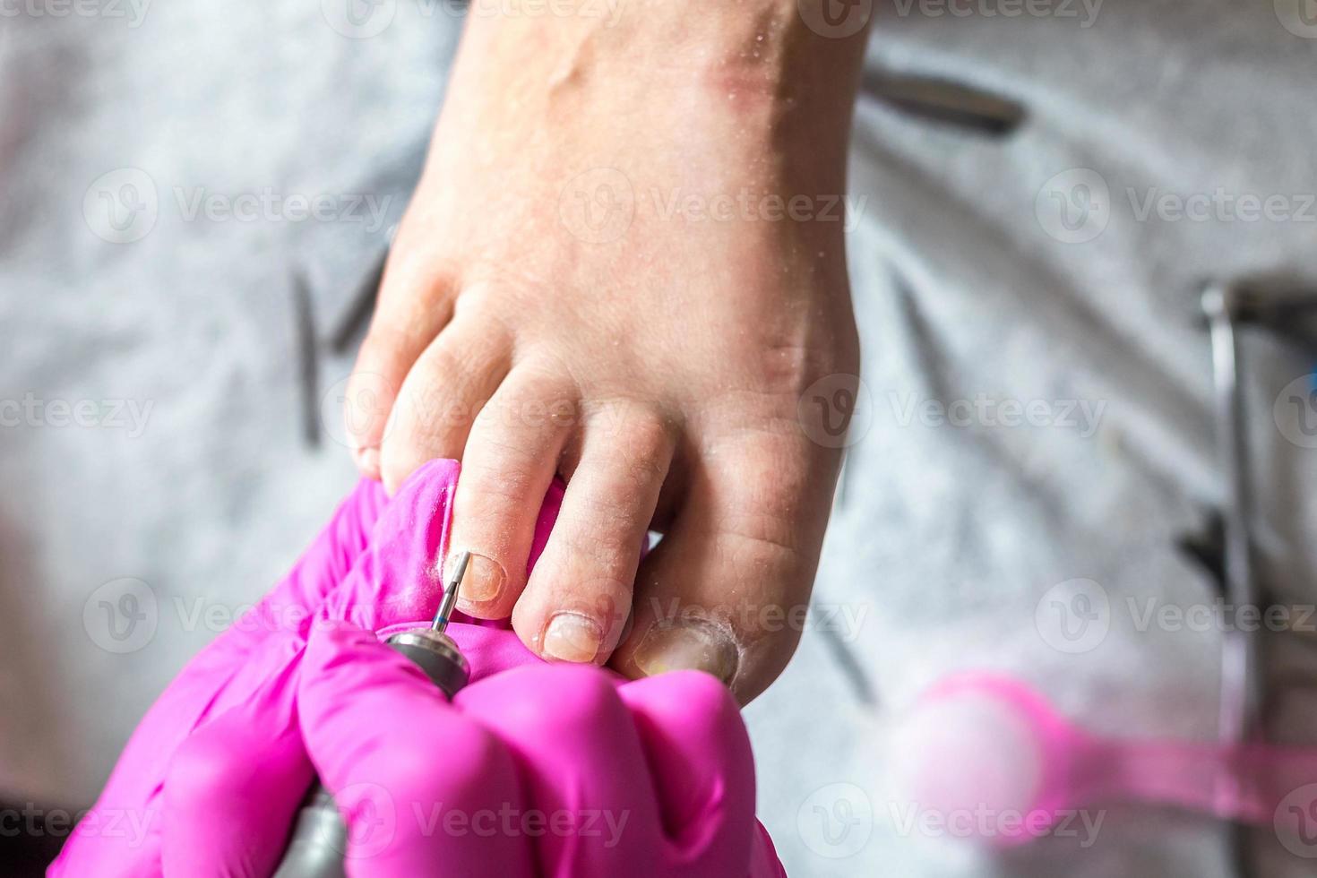 Pedicurist master in pink gloves cuts the cuticle and shellac toe nails in the pedicure salon using drill.  Professional pedicure in cosmetology clinic. Hygiene for feet in beauty salon. photo