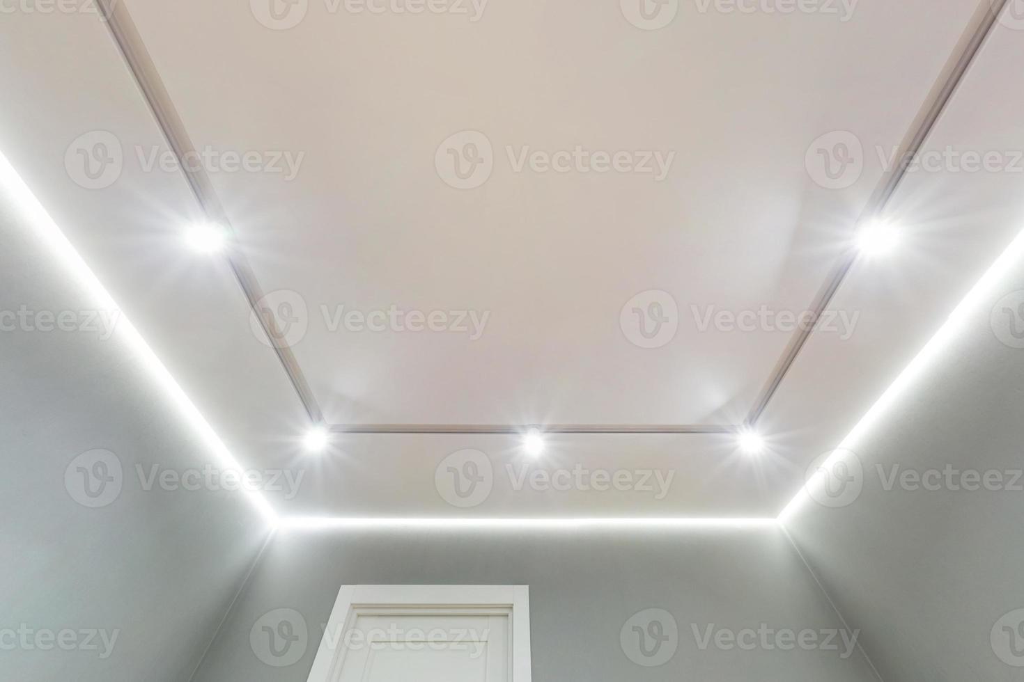 looking up on suspended ceiling with halogen spots lamps and drywall construction in empty room in apartment or house. Stretch ceiling white and complex shape. photo