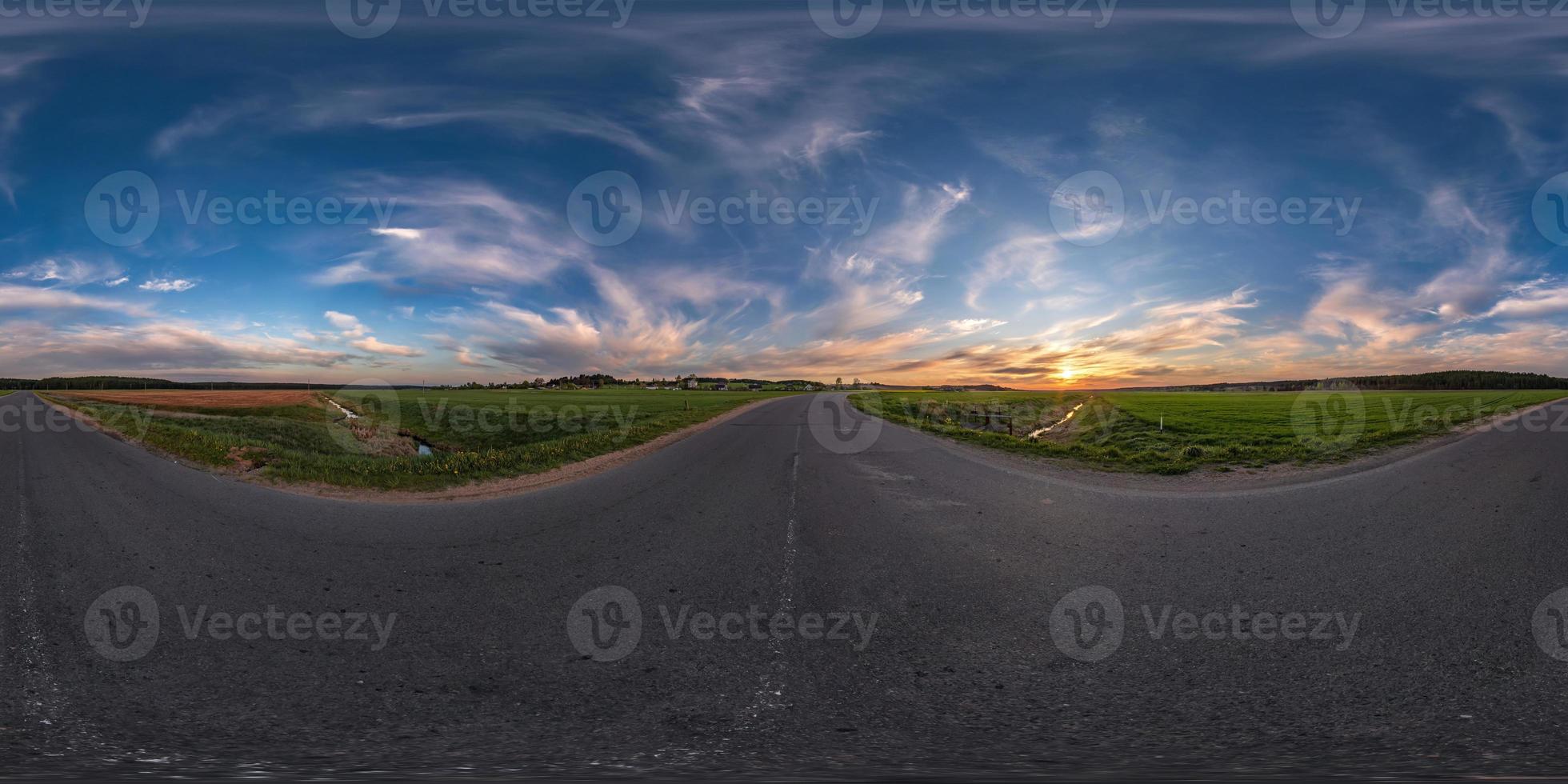 Full spherical seamless panorama 360 degrees angle view on old no traffic asphalt road among fields in evening  before sunset with cloudy sky in equirectangular projection, VR AR content photo