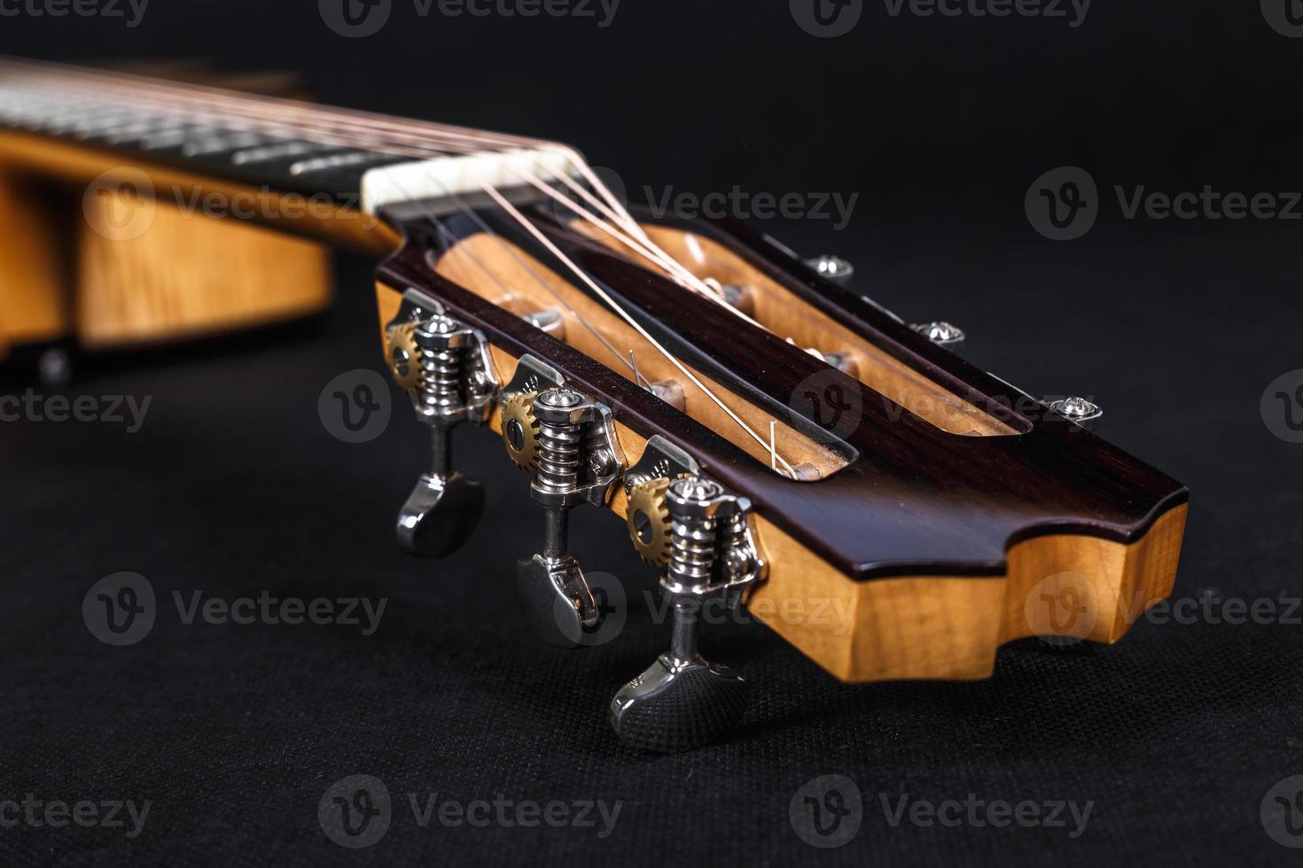 Tuning pegs on wooden machine head of six strings acoustic guitar neck on black background photo