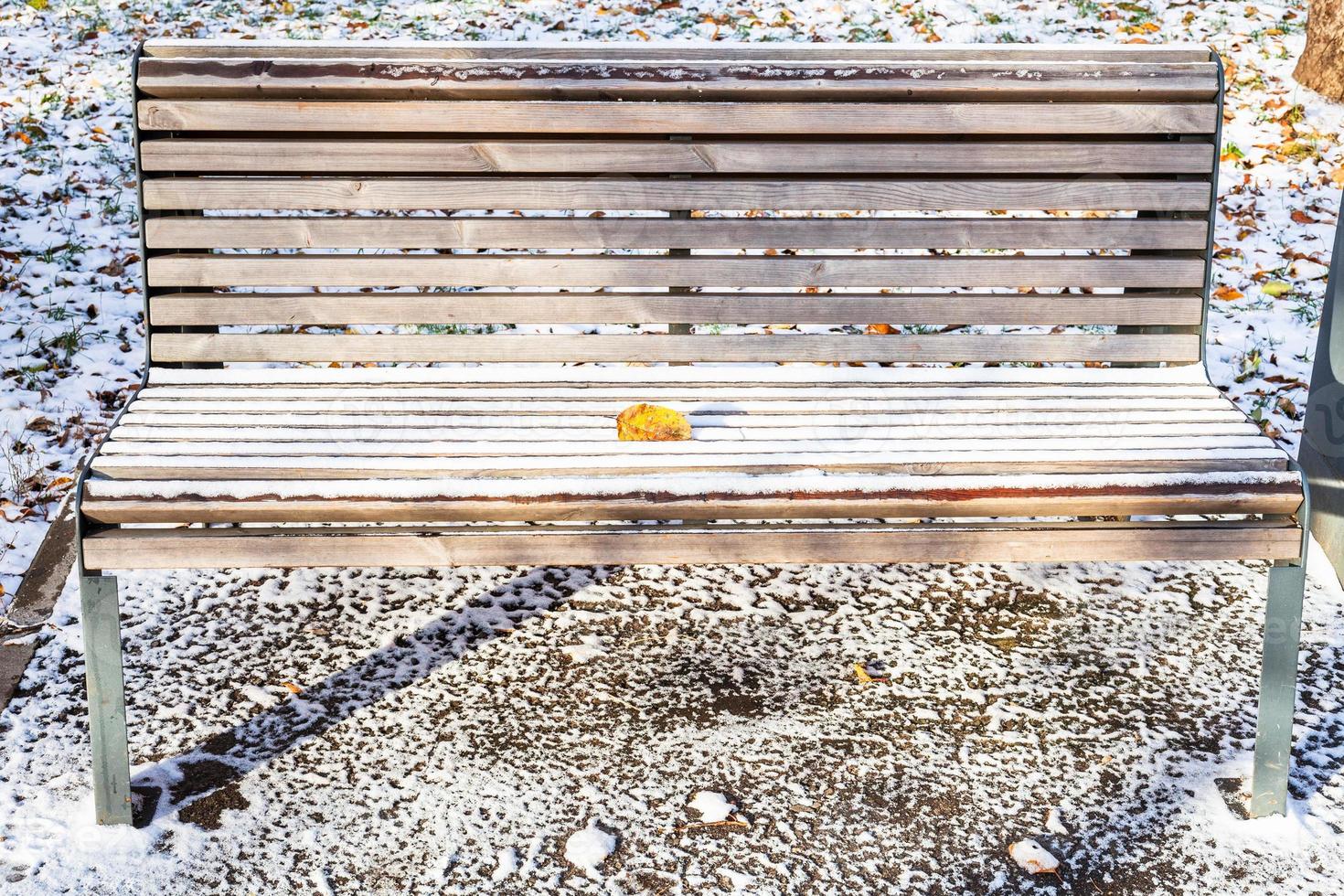 wooden bench with fallen leaf covered with snow photo