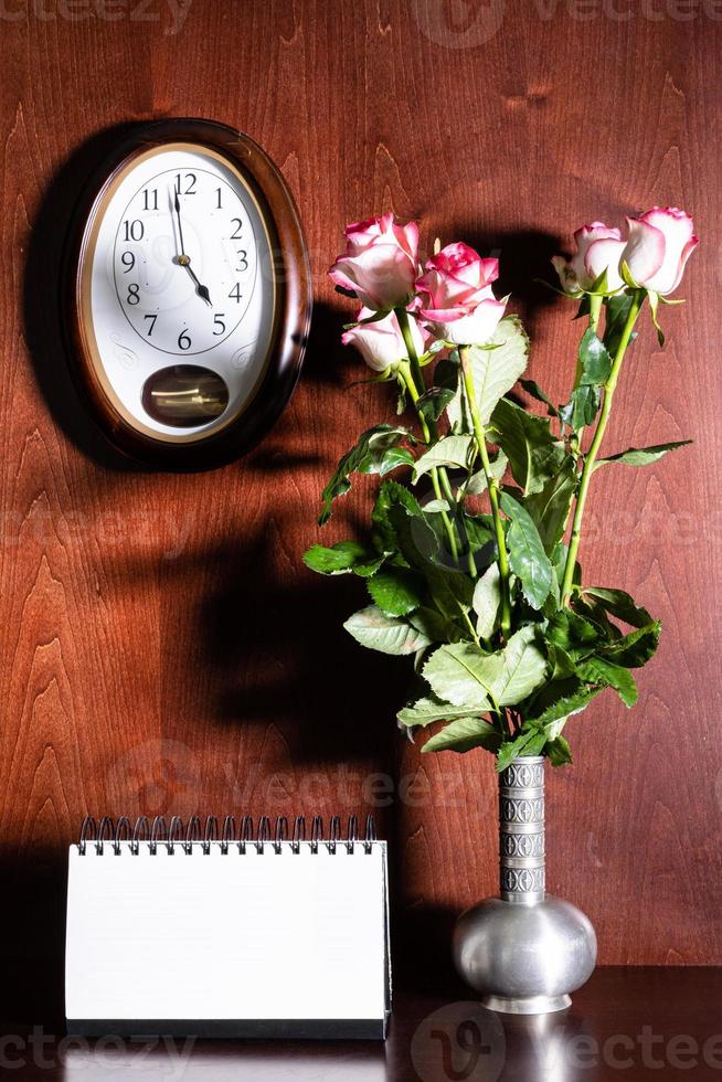 reloj de pared, calendario en blanco y rosas rosas en jarra foto