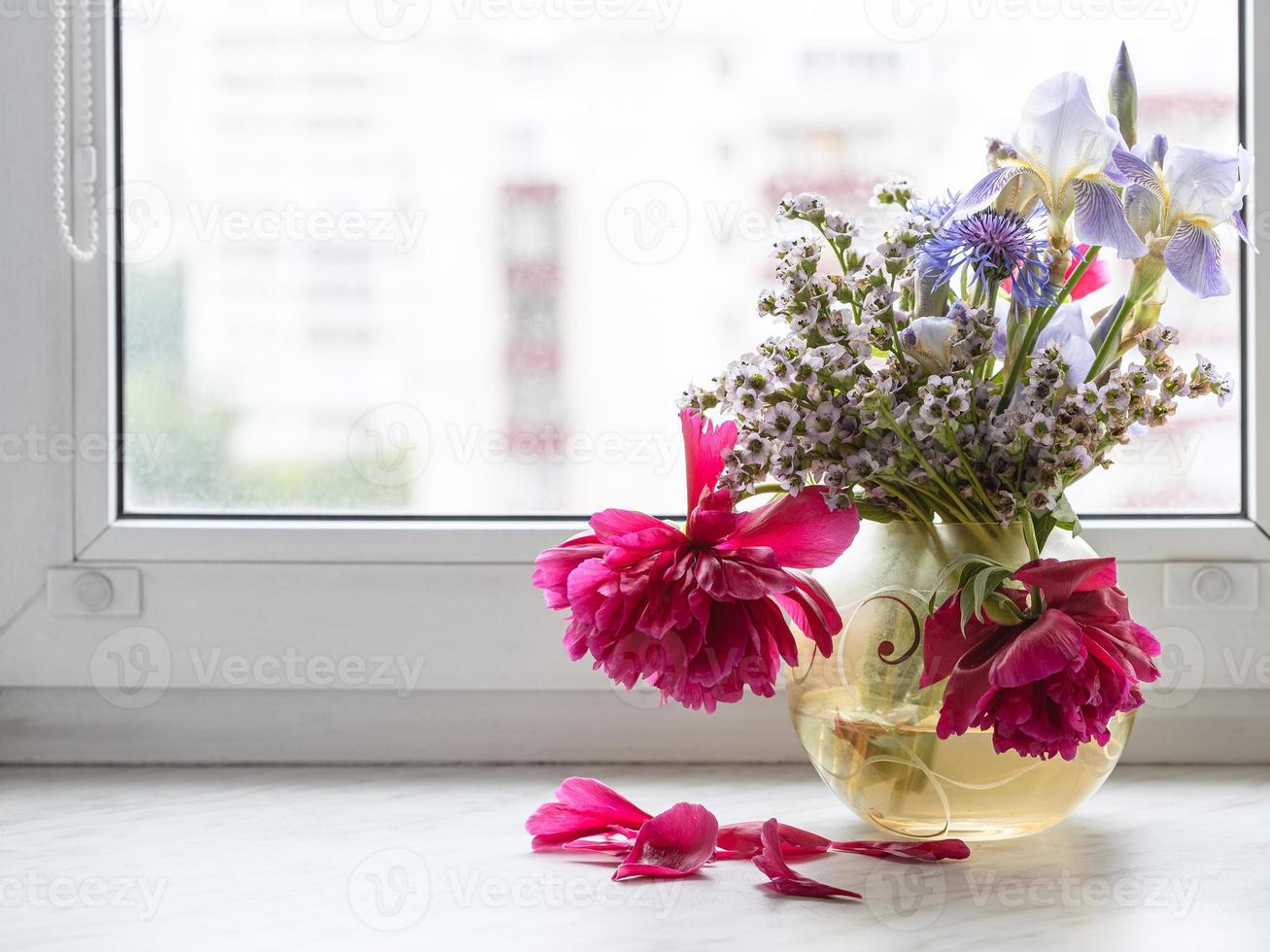 various flowers in glass vase on window sill photo