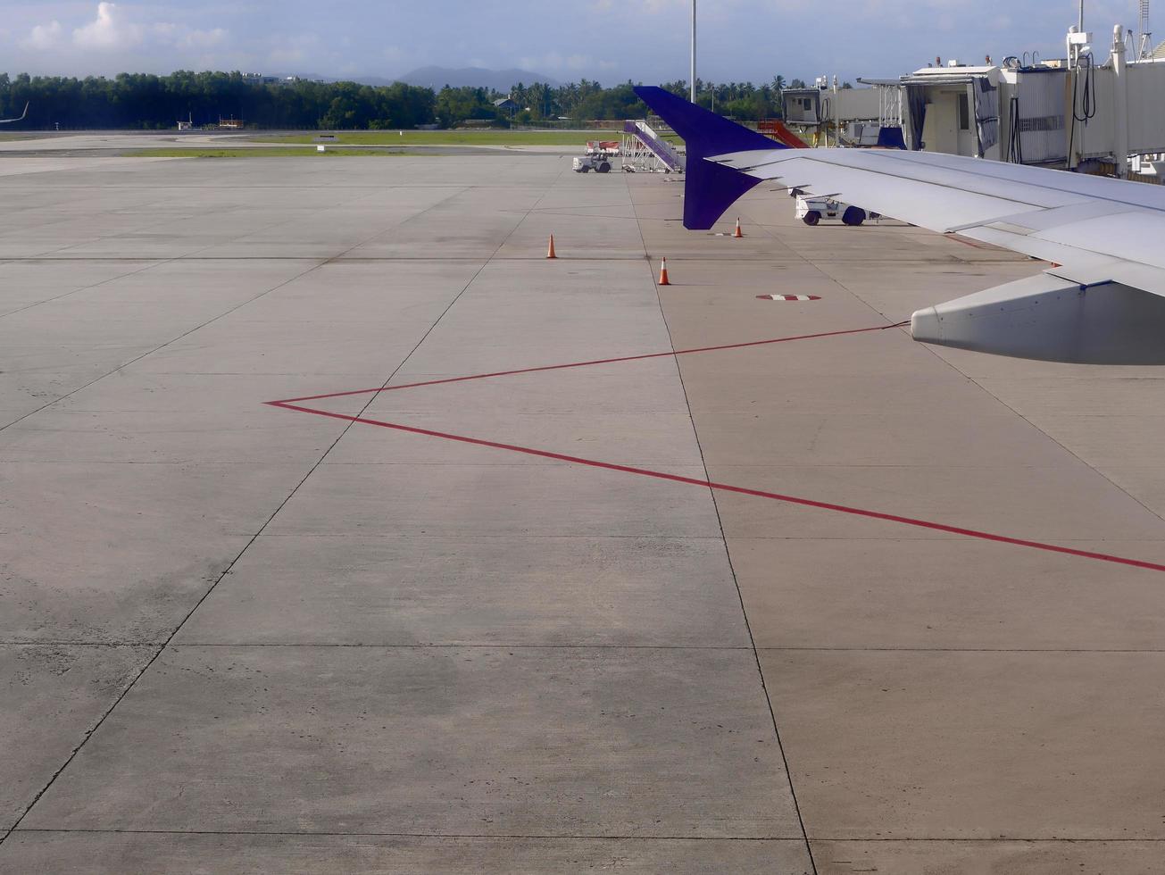Airplane wing with docked ladder at the airport field apron, taxiway with red line marking photo