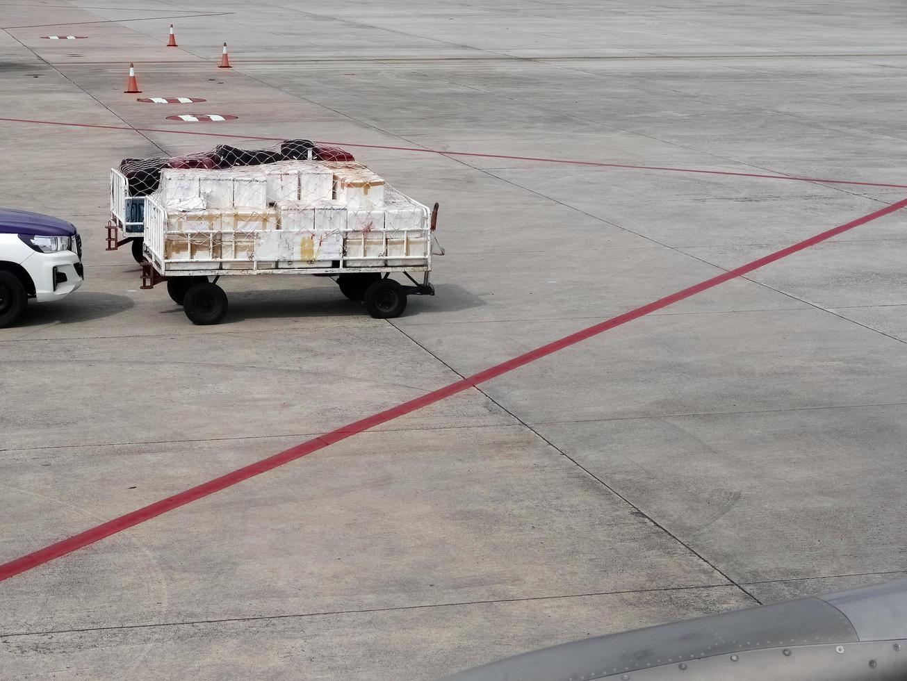 equipaje de servicio en tierra y paquete en carrito de carro que se entrega al avión en la calle de rodaje con la línea roja marcada en el aeropuerto. foto