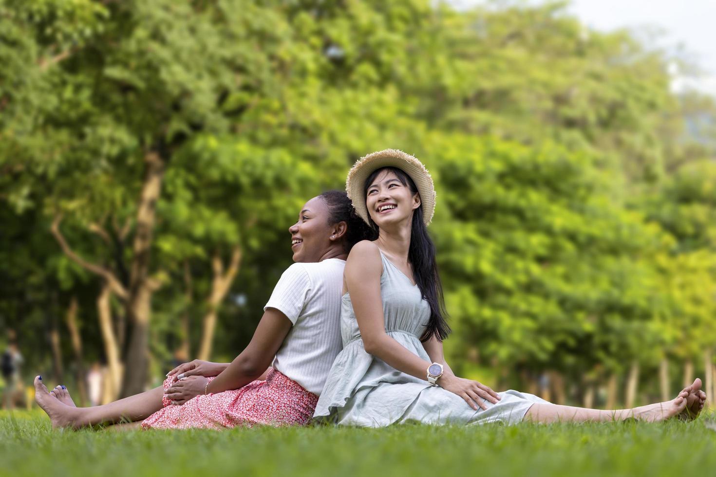 Diversity of LGBTQ lesbian couple is relaxingly sitting together on the grass lawn in public park during summer season to enjoy the leisure time concept photo