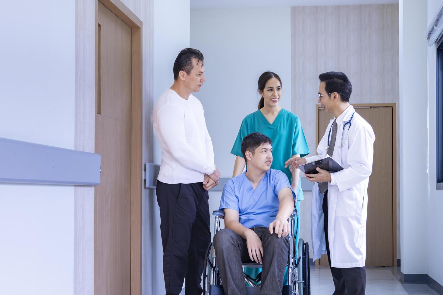 el equipo de médicos está discutiendo con la enfermera y los padres sobre el niño paciente en silla de ruedas en su cita en el hospital para fisioterapia después de una cirugía de rodilla por accidente foto