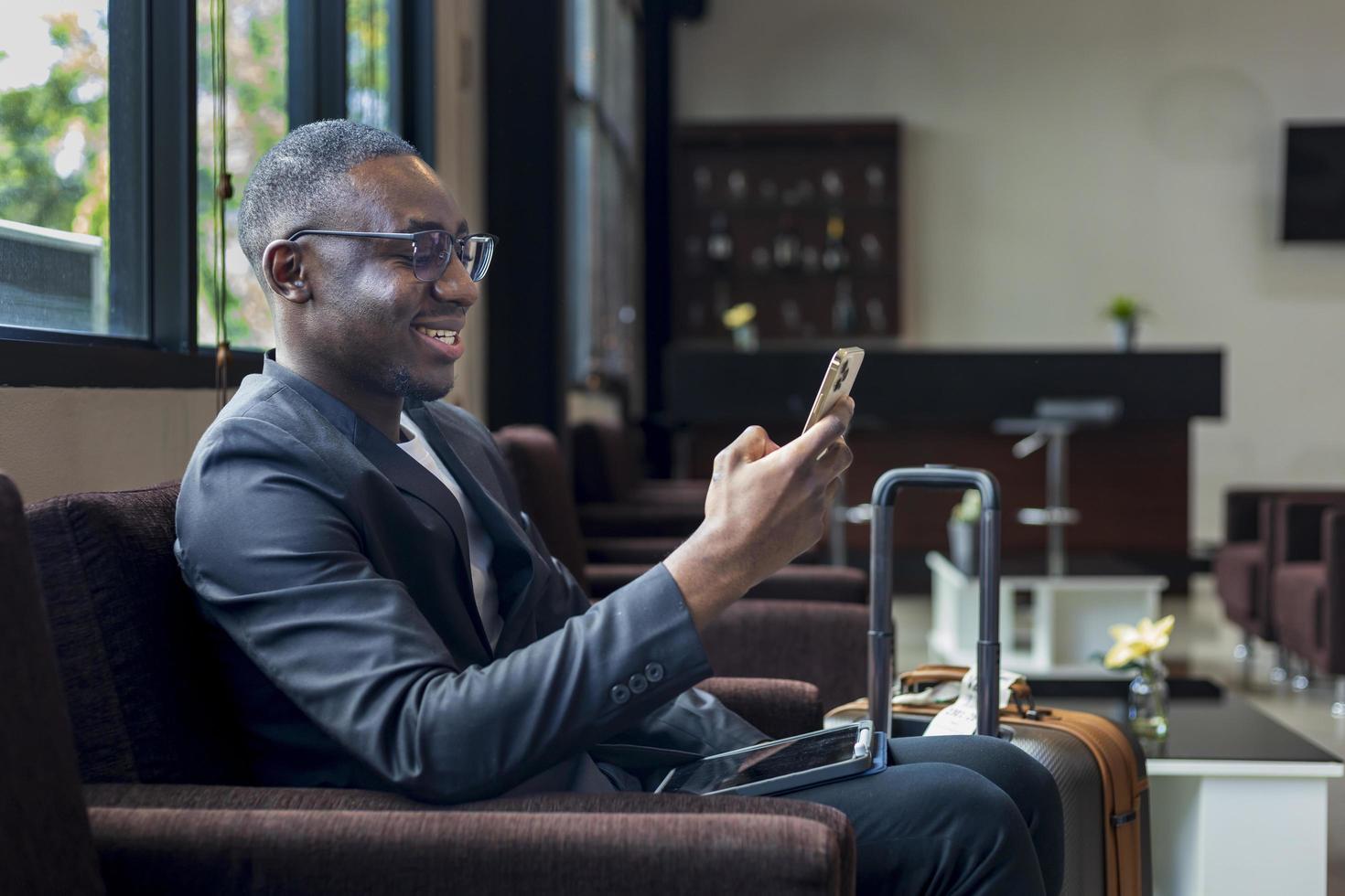 African American businessman is using mobile phone for video call while waiting in airline business departure lounge waiting for boarding the airplane photo