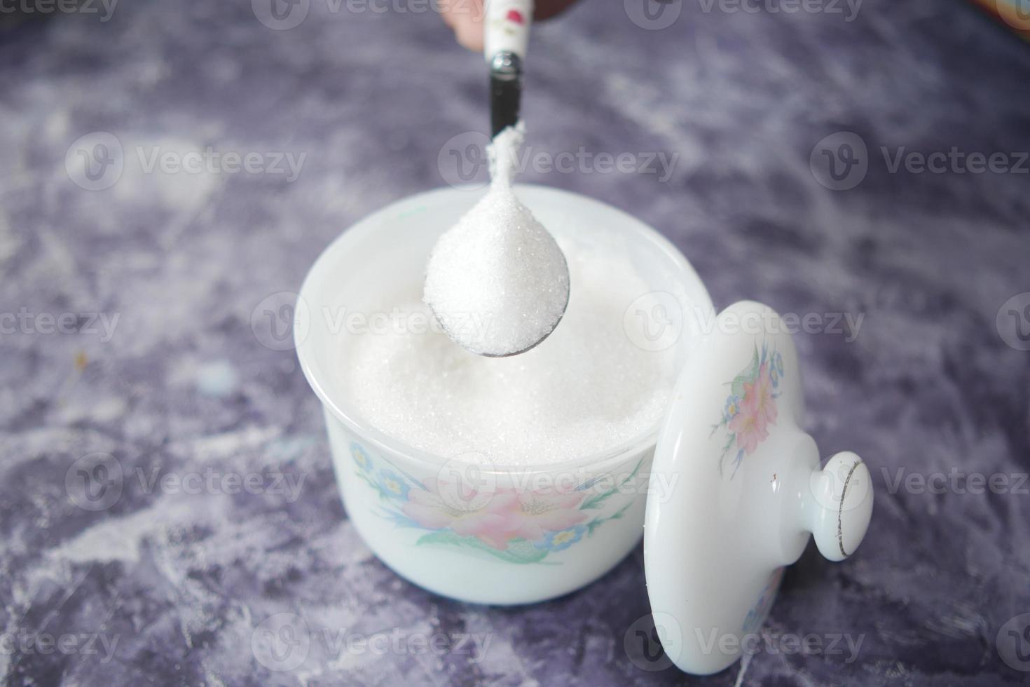 white sugar and spoon in a container on black background, photo