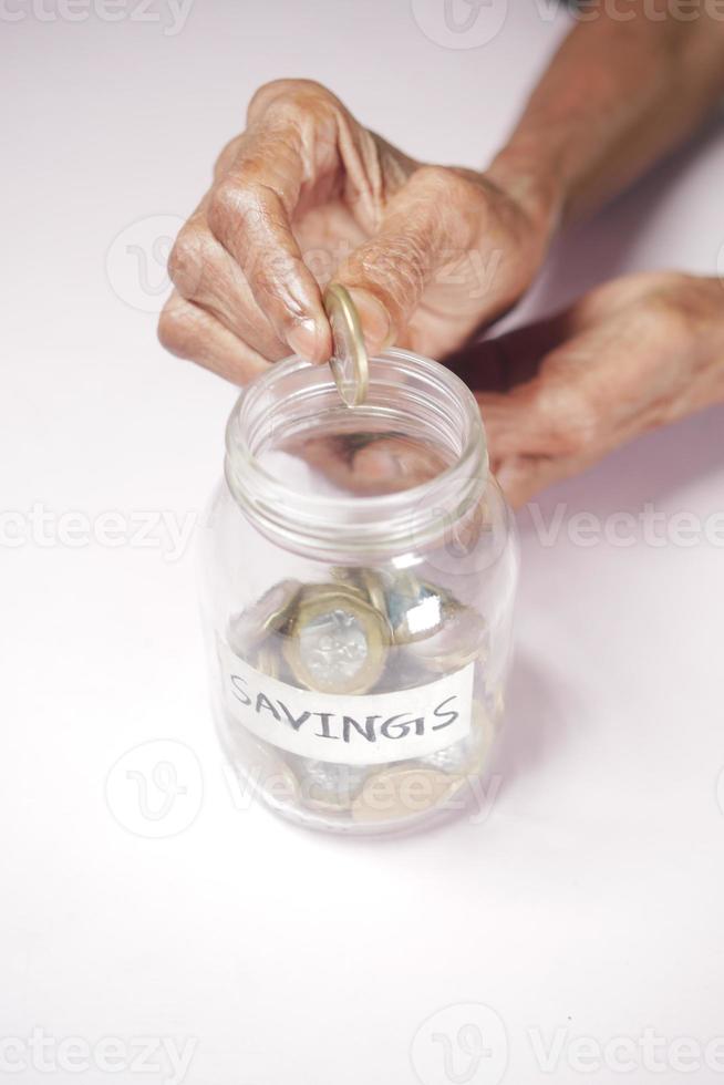 senior women saving coins in a jar white sited photo