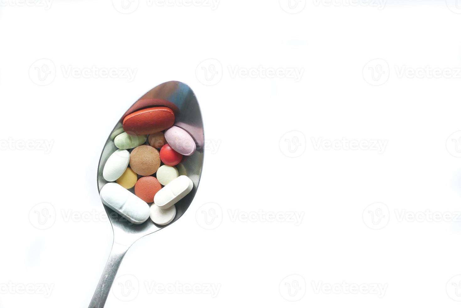 Close up of many colorful pills and capsules on a spoon isolated on white photo