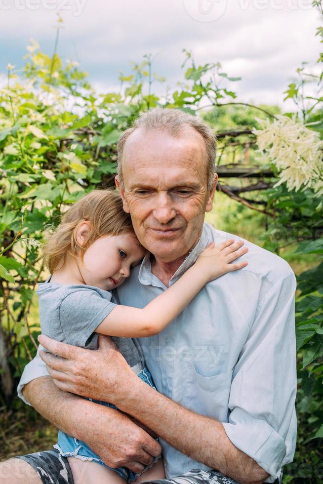 A little girl hugs her grandfather on a walk in the summer outdoors. photo