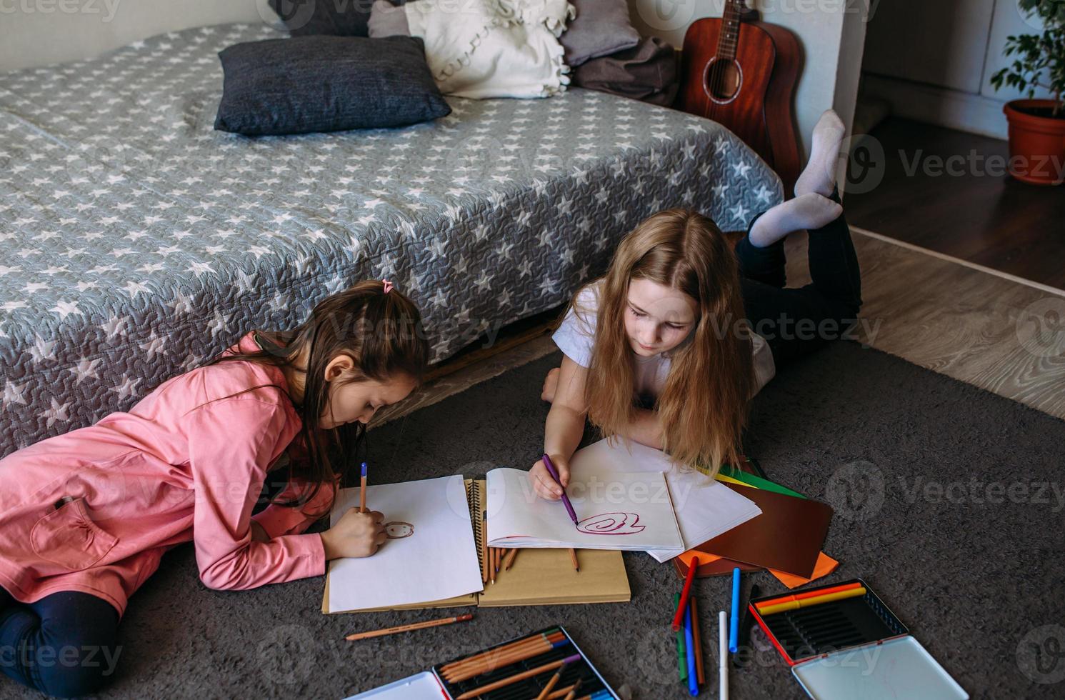 Two girls friends play at home, draw with pencils and felt-tip pens and have fun photo