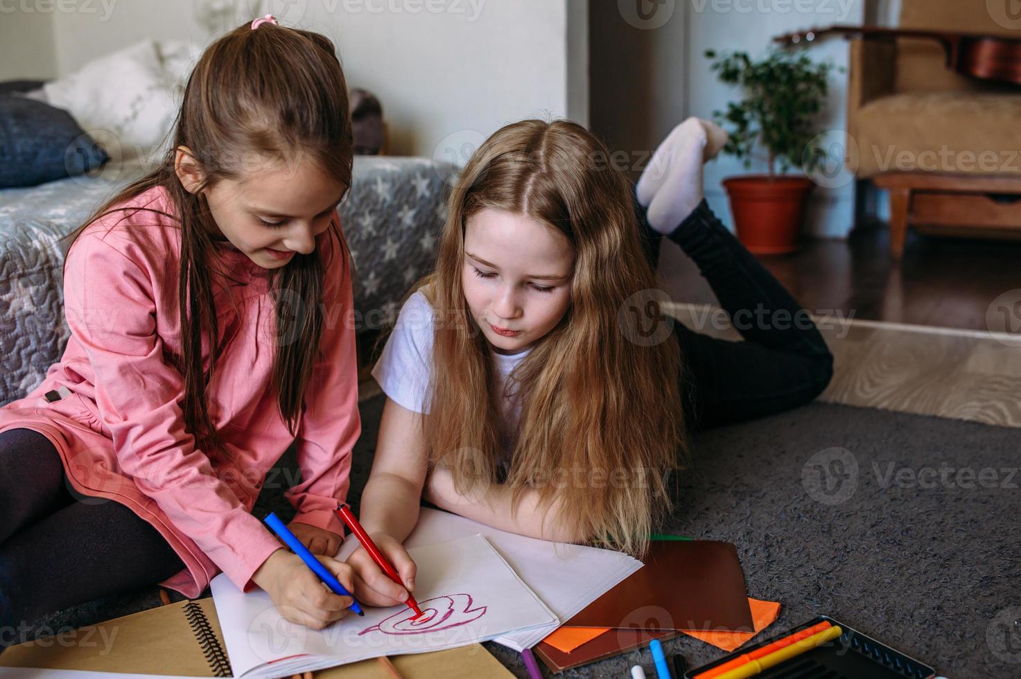 Two girls friends play at home, draw with pencils and felt-tip pens and have fun photo