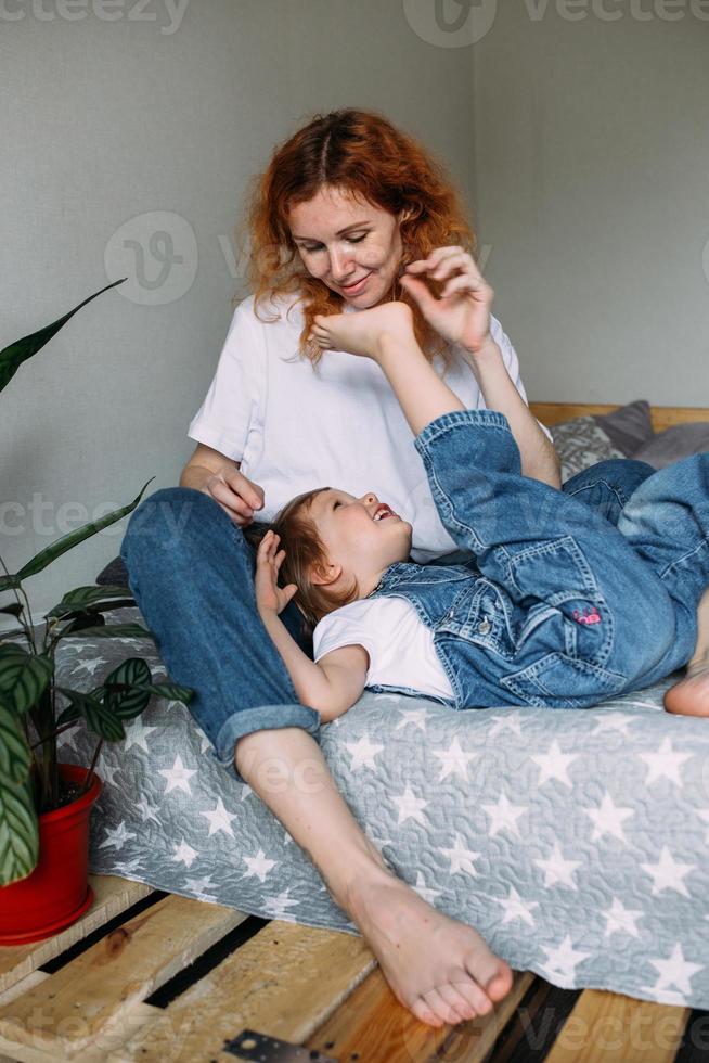 Young mother and child have fun and fool around at home on the bed photo