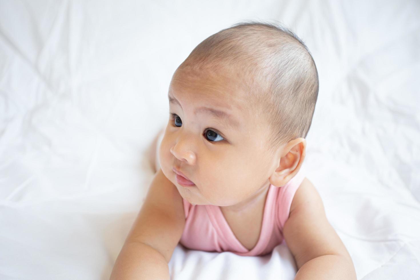 Asian cute baby in white sunny bedroom. Newborn child relaxing on bed photo