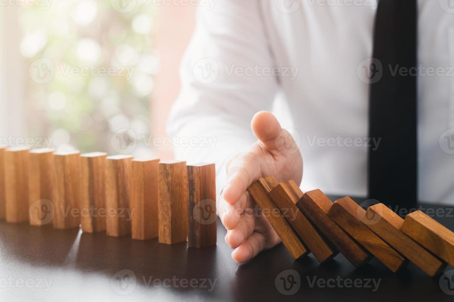 gestión de riesgos, la mano del hombre de negocios detiene la caída continua de dominós de madera, detiene el impacto de la crisis empresarial. cobertura para resolver problemas de negocios para el éxito. foto