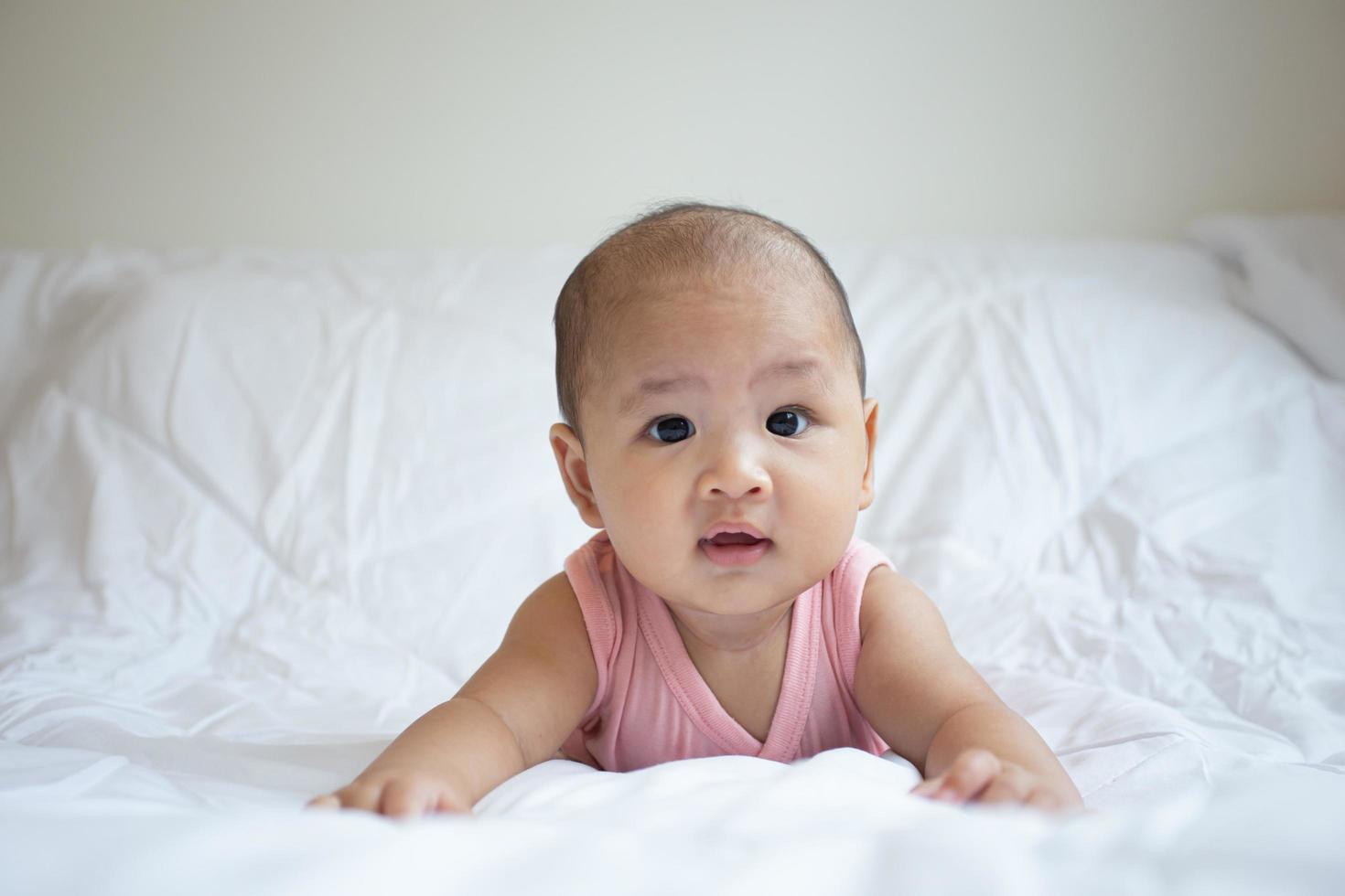 Asian cute baby in white sunny bedroom. Newborn child relaxing on bed photo