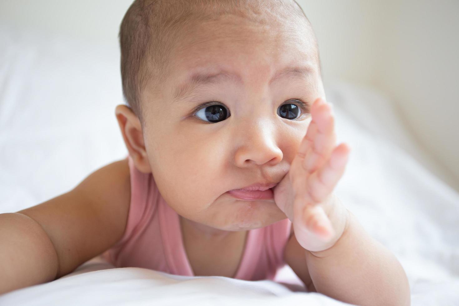 Asian cute baby in white sunny bedroom. Newborn child relaxing on bed photo