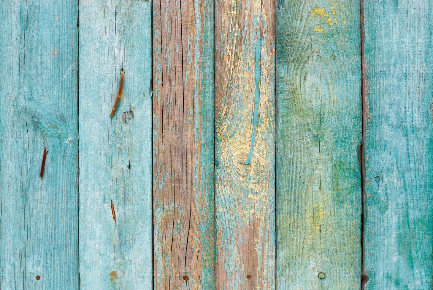 The texture of an old wooden fence with weathered boards painted with peeling paint in a muted emerald green color. photo