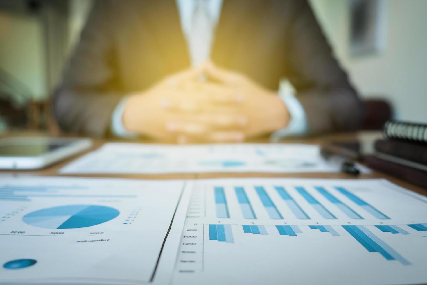 documentos comerciales en la mesa de la oficina con un diagrama financiero gráfico y un hombre de negocios trabajando en segundo plano. foto