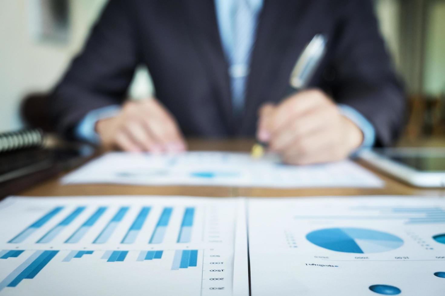 Handsome young man working with touchpad while sitting on the couch in office and financial statistic graph, blurred background. photo